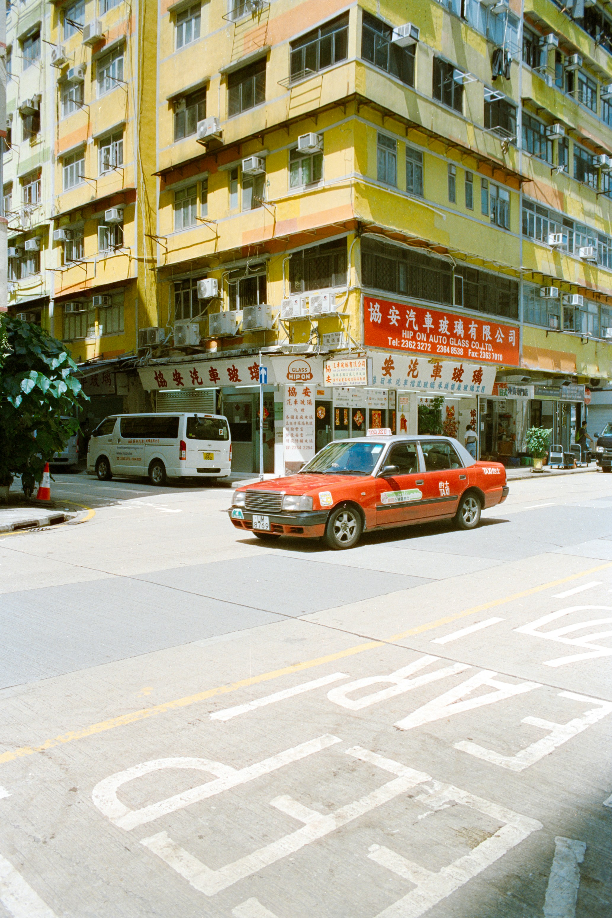 A red taxi driving past a yellow apartment building in Hong Kong