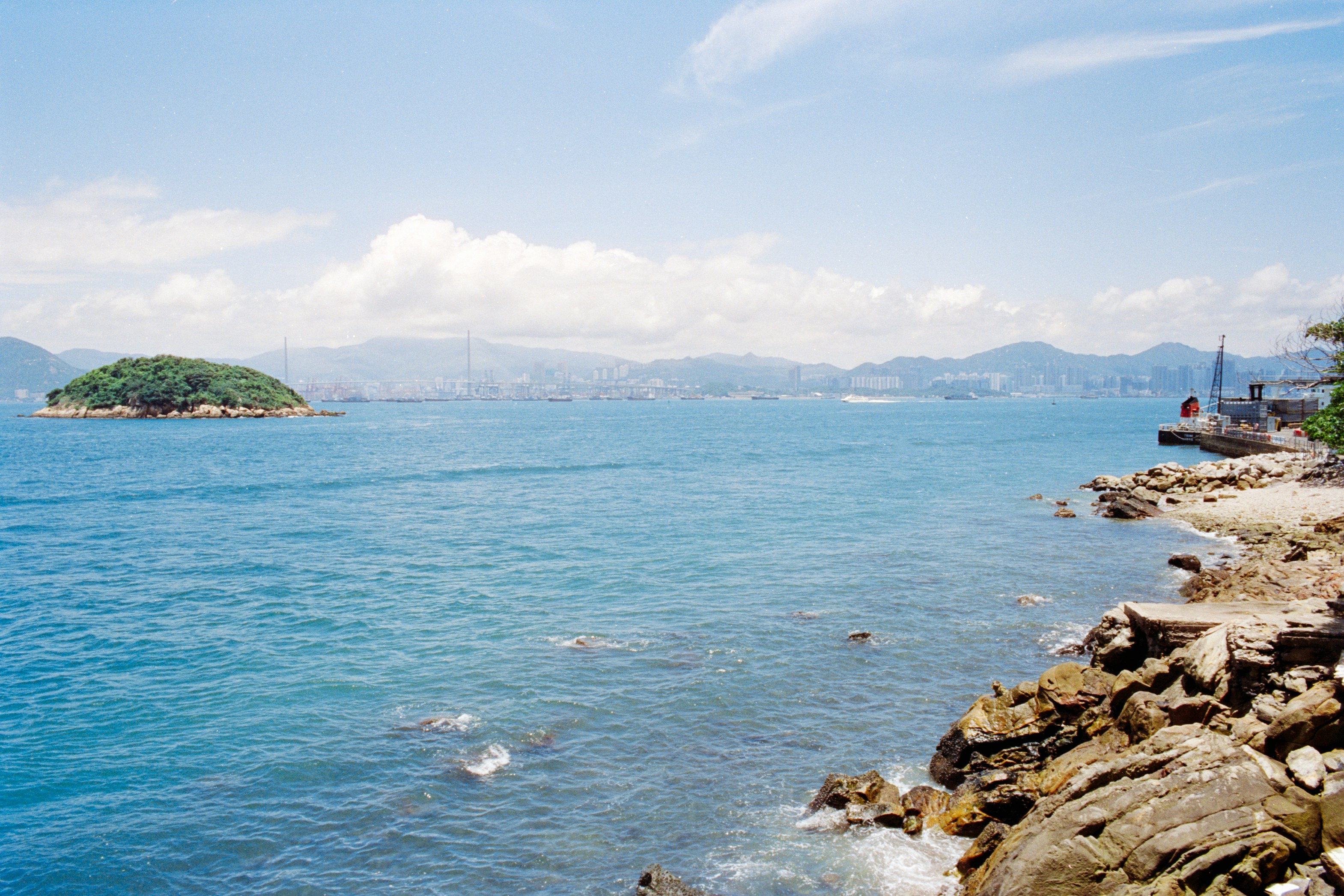 A small green island in the blue sea near a rocky coastline in Hong Kong