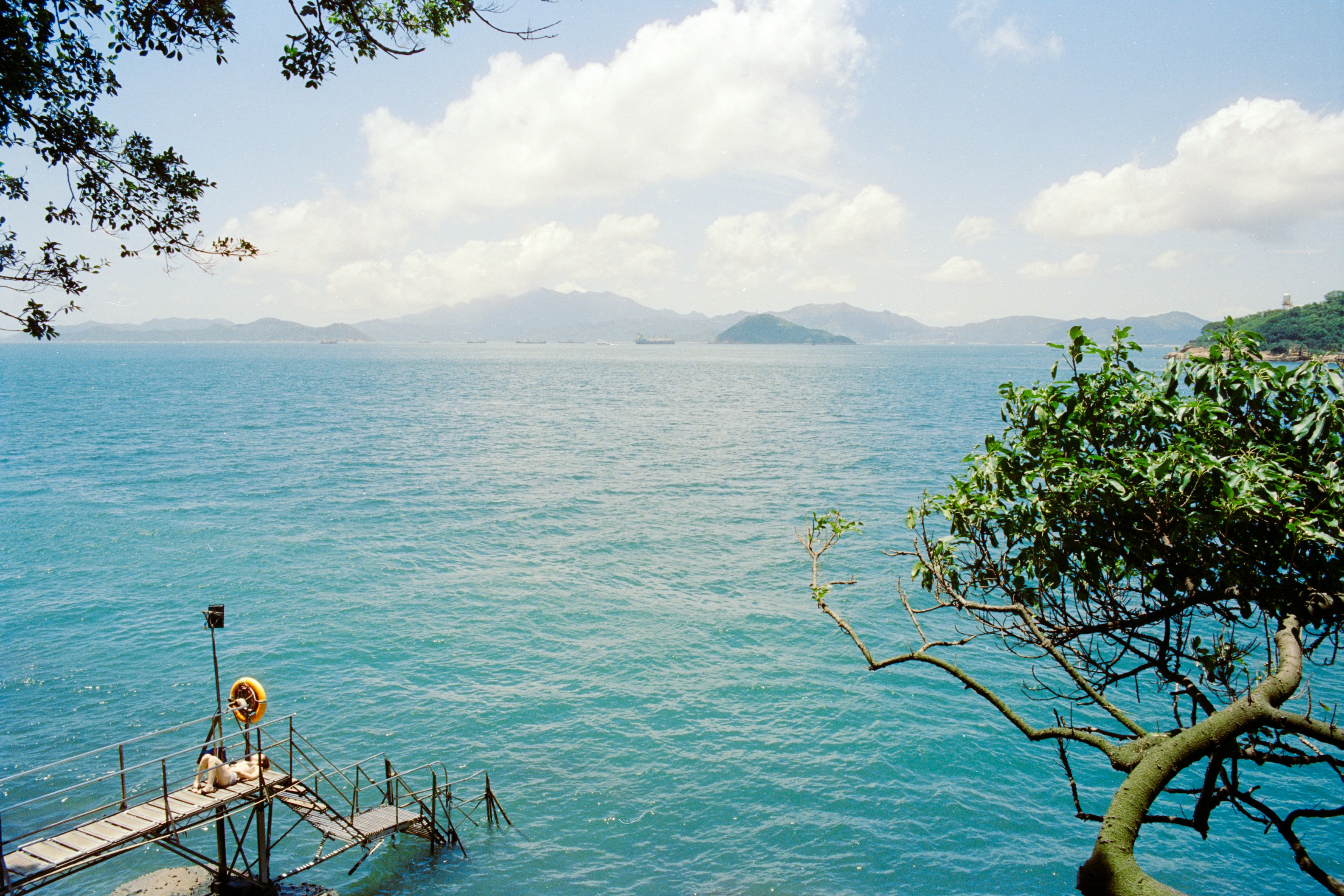 A person lying on a metal pier extending into a blue sea with distant mountains