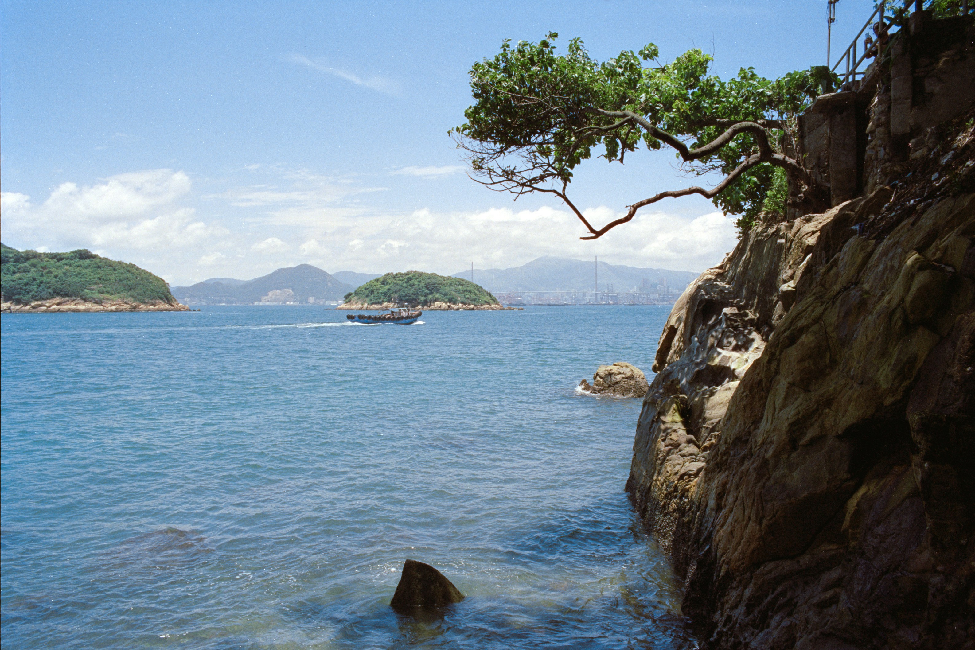 A small boat crossing blue water between rocky islands under a clear sky