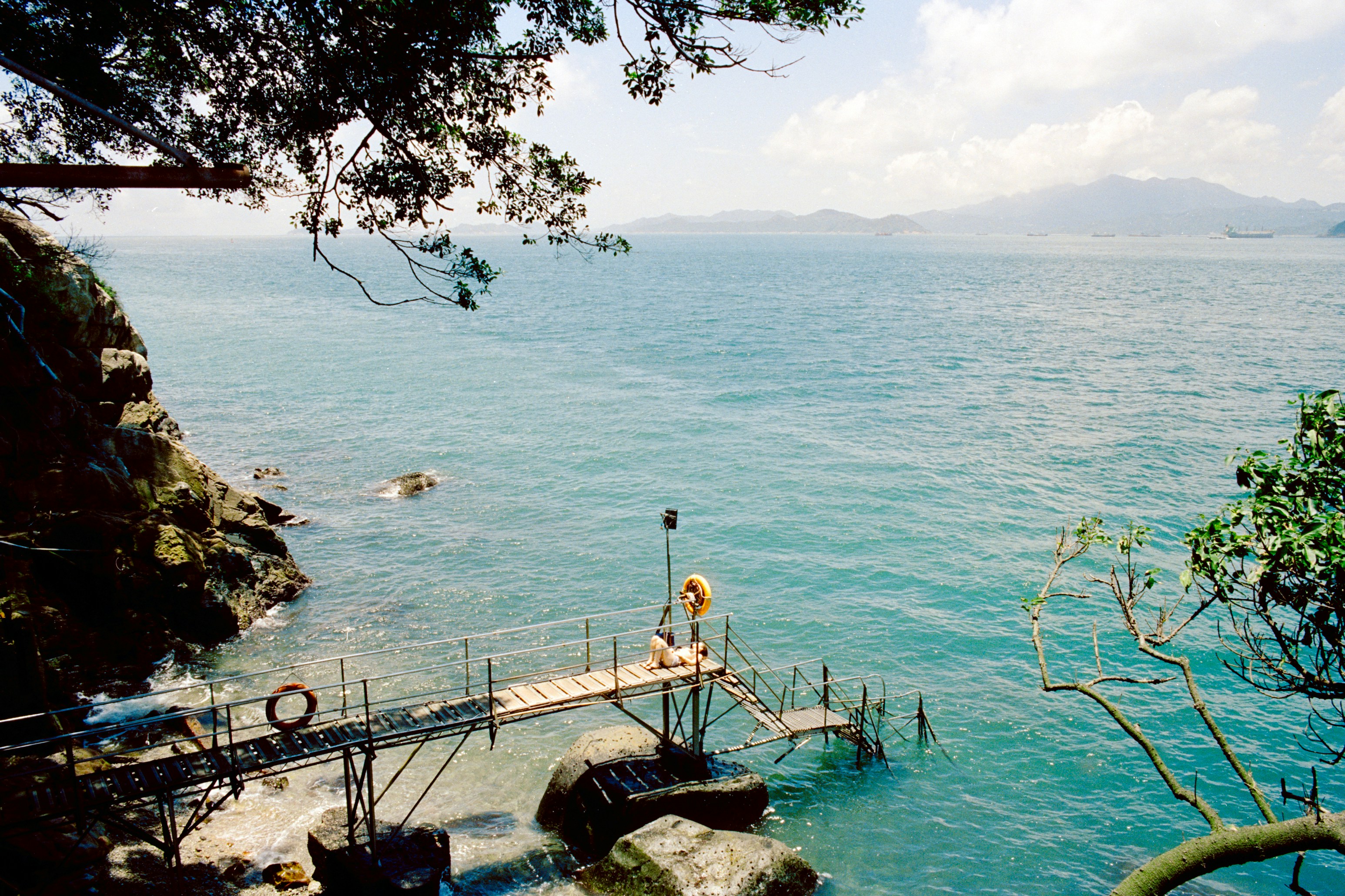 A metal pier extending over blue water from a rocky cliffside