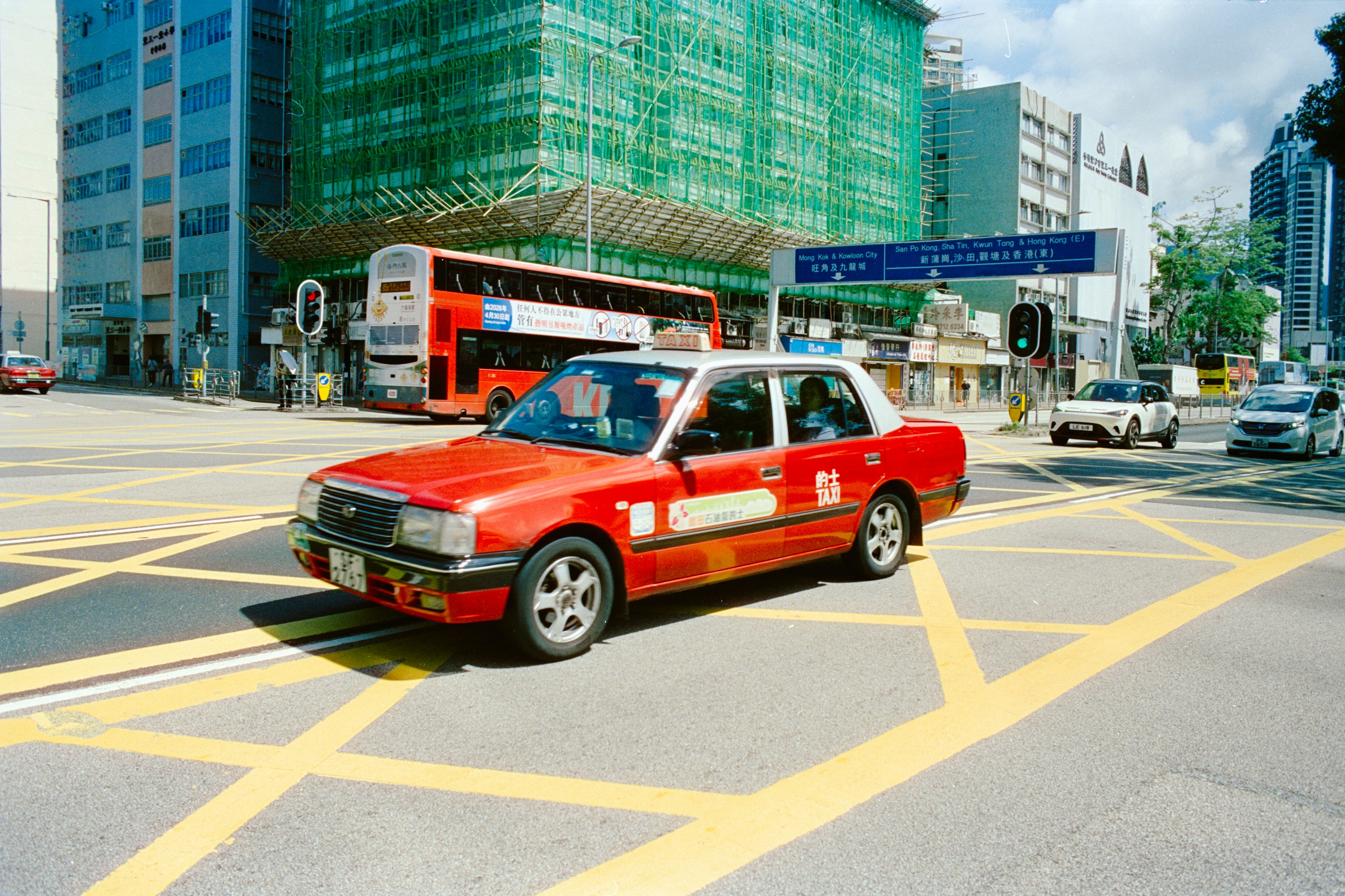 A red taxi driving through a yellow grid intersection in Hong Kong