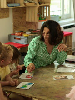 A woman in a green patterned shirt pointing at clay shapes with two children