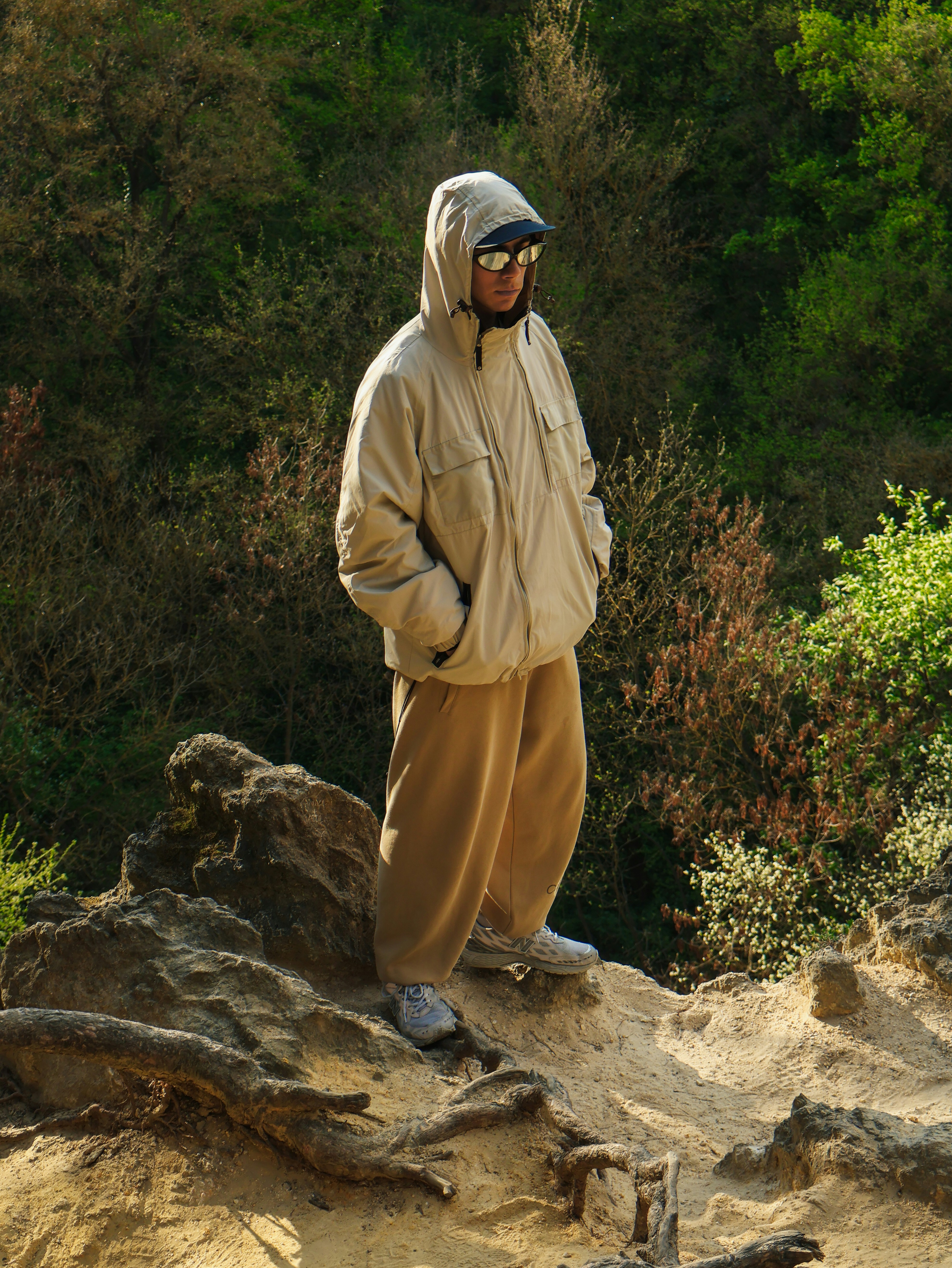A person in a beige hooded jacket and tan pants on a rocky outcrop