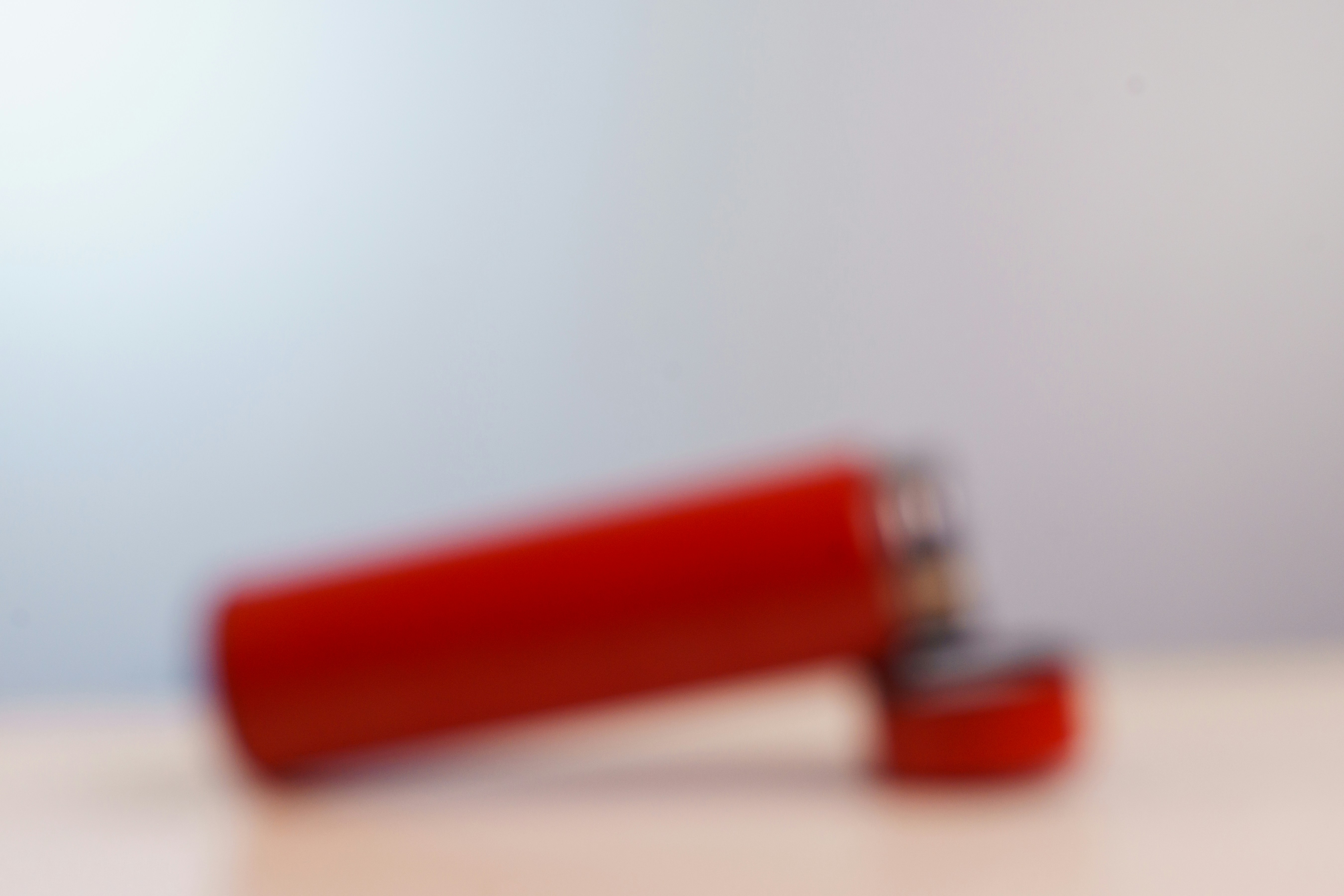 A blurred red cylindrical object with a cap on a light surface