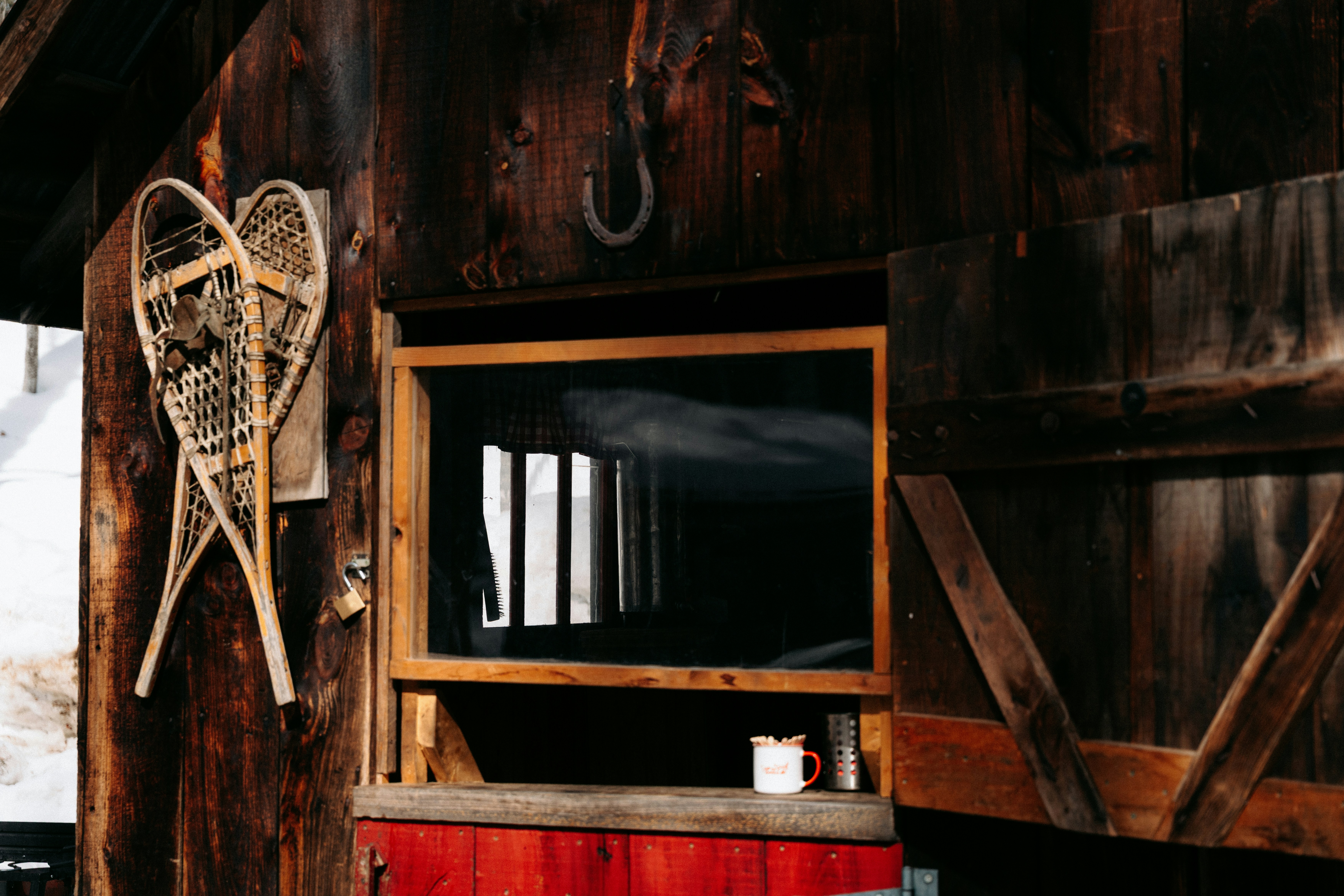 Wooden snowshoes hanging on a dark timber wall beside a window and mug
