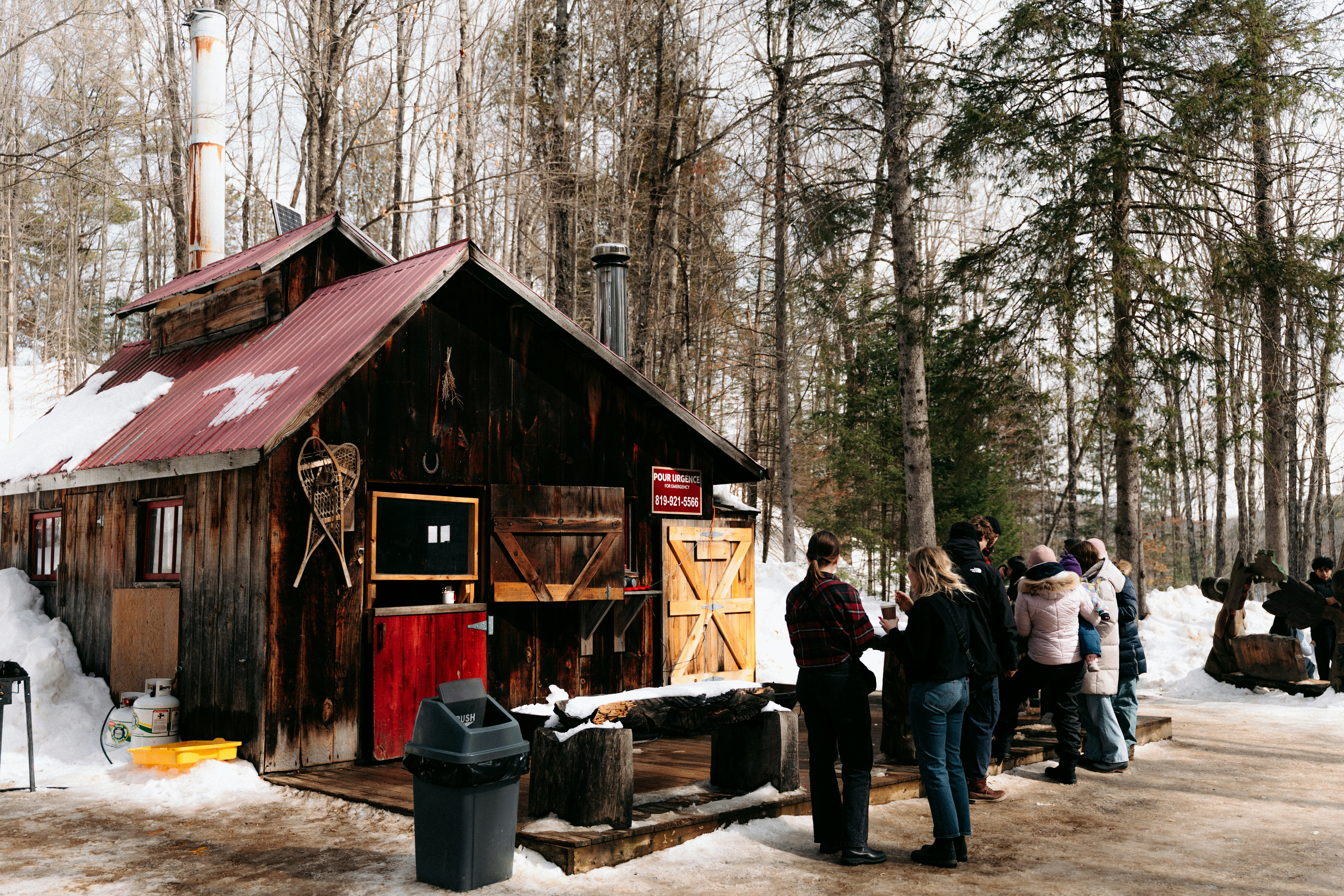 A group of people standing outside a rustic wooden sugar shack in winter