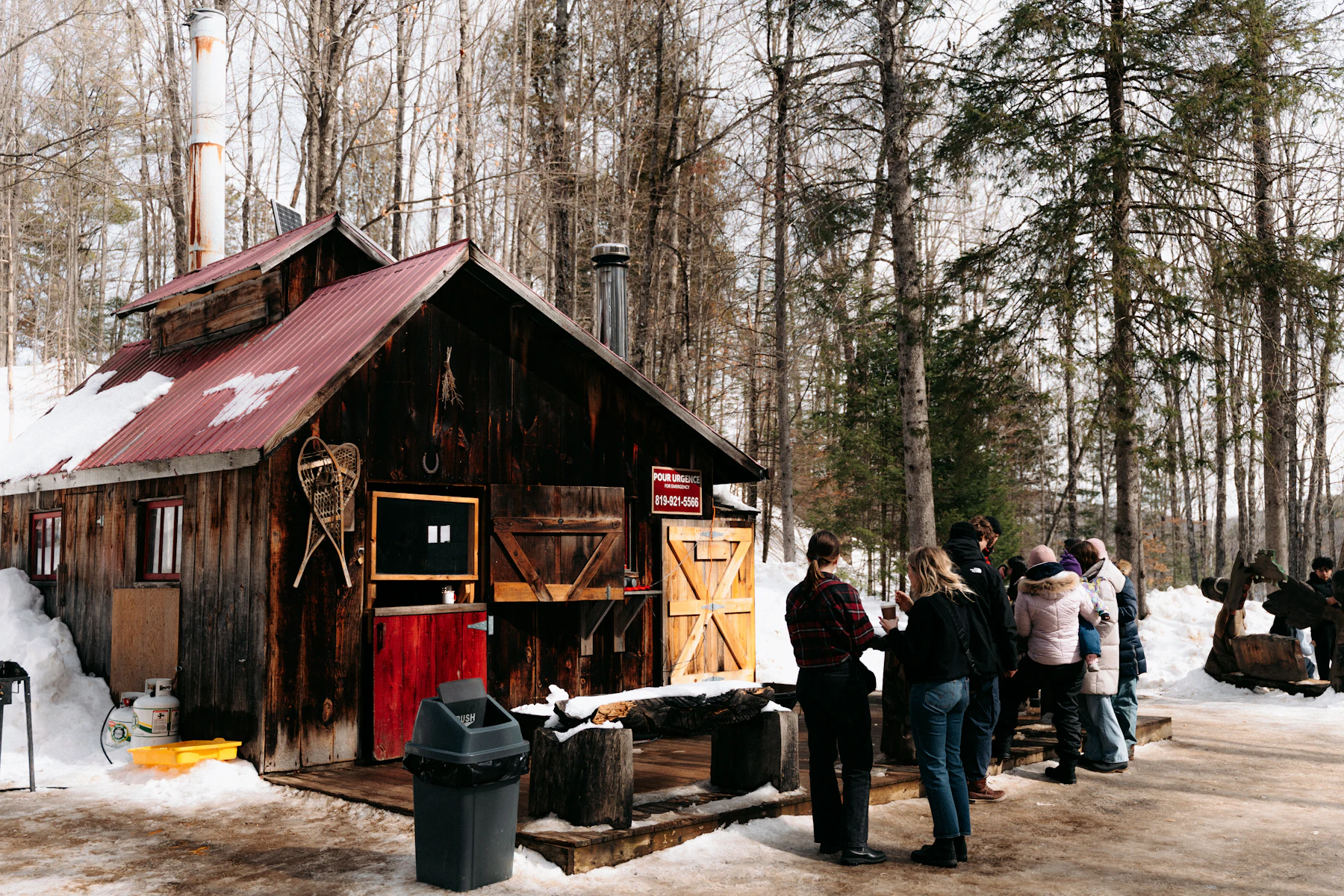 Visitors in winter coats outside a rustic wooden sugar shack on an open-house day