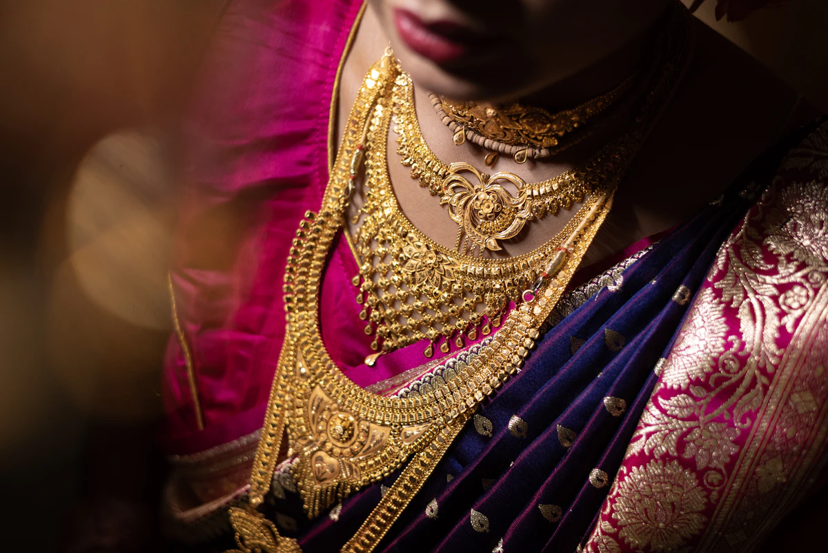 Bride wearing a stacked gold choker, a filigree bib necklace and a long haar over a purple and magenta Banarasi sari