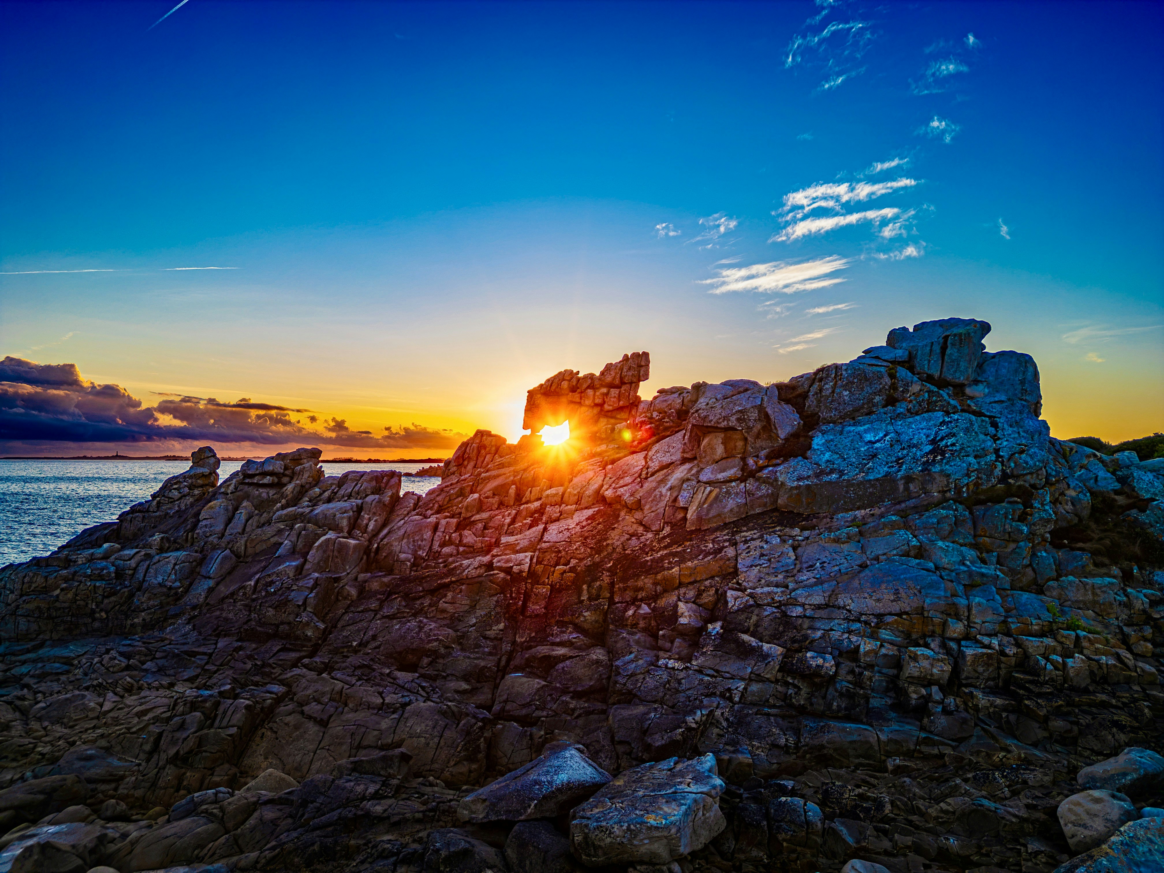 Low sun shining through a gap in jagged coastal rocks at the water edge