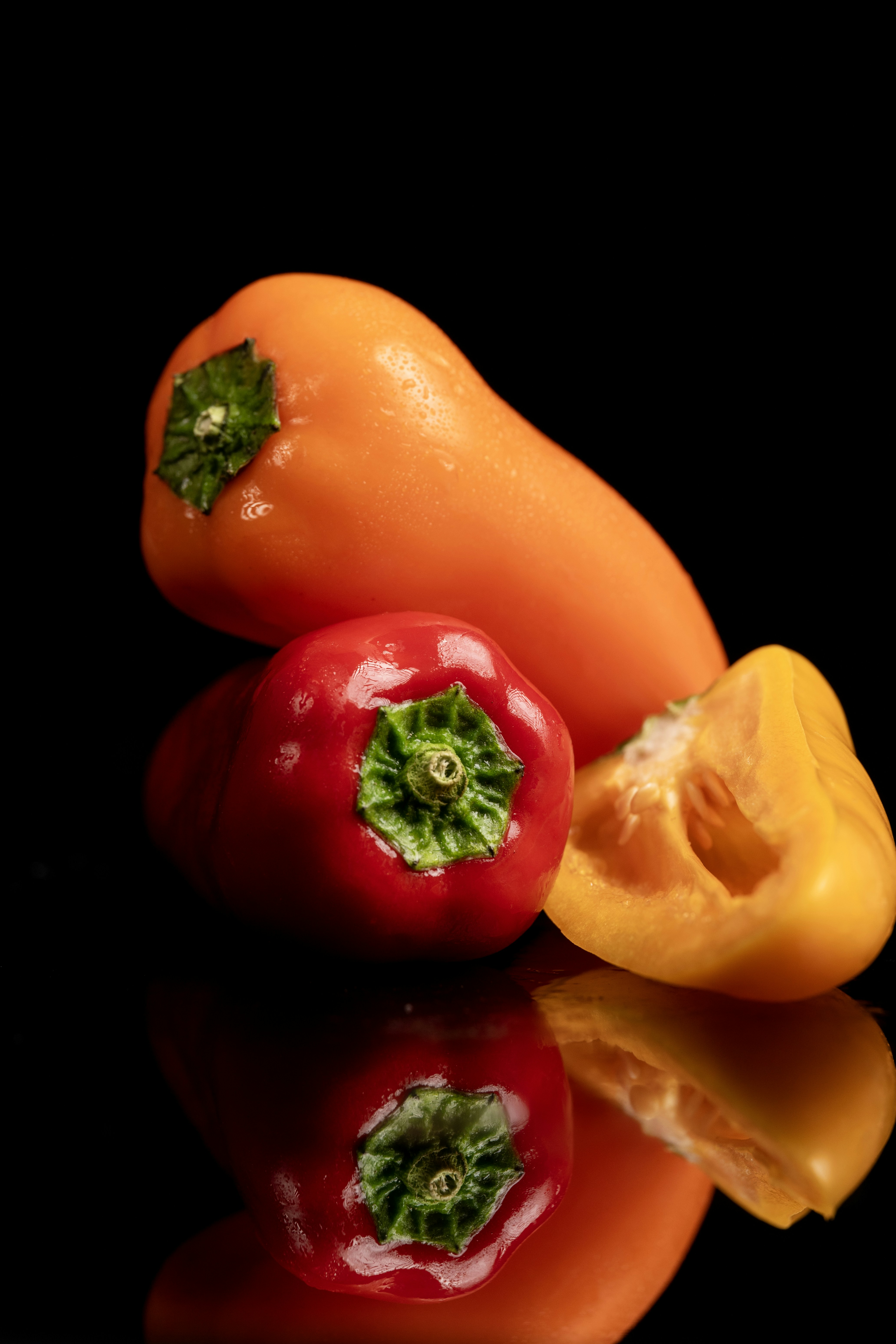 An orange pepper, a red pepper, and a yellow pepper slice on a black surface