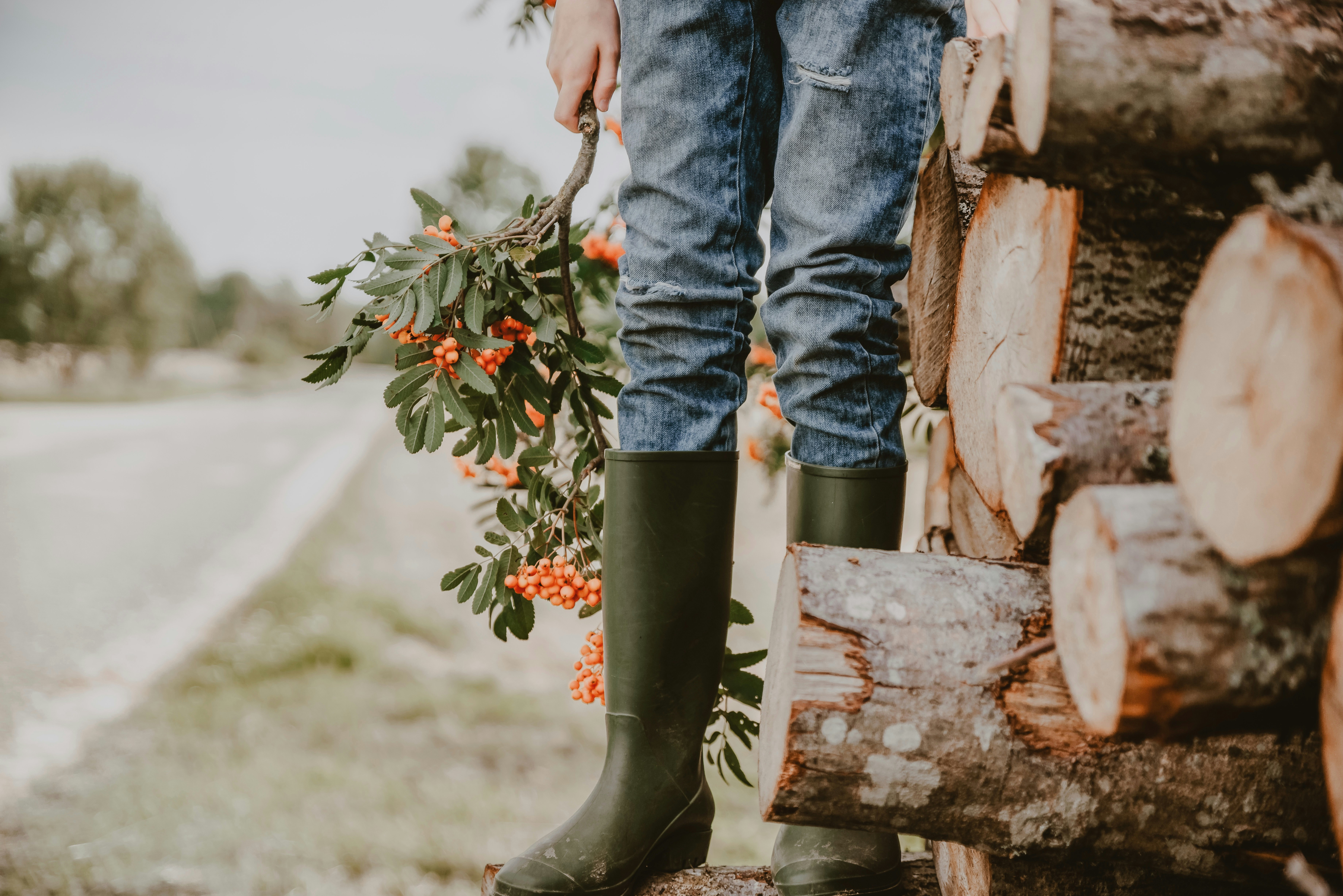 Photo of A person in blue jeans and green rubber boots holding a rowan branch by Anita Austvika