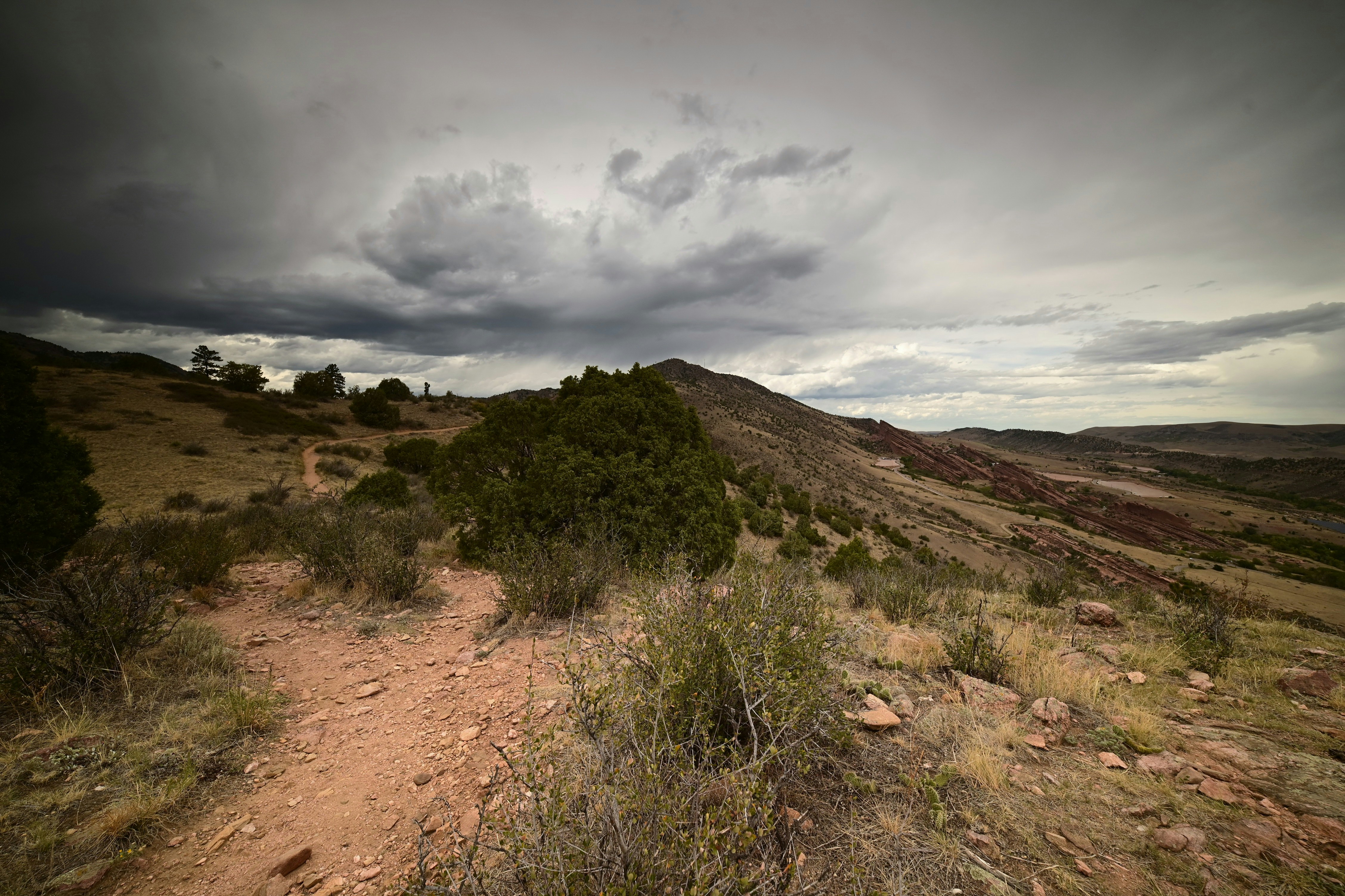 A dirt hiking trail winding through a hilly landscape under a dark cloudy sky