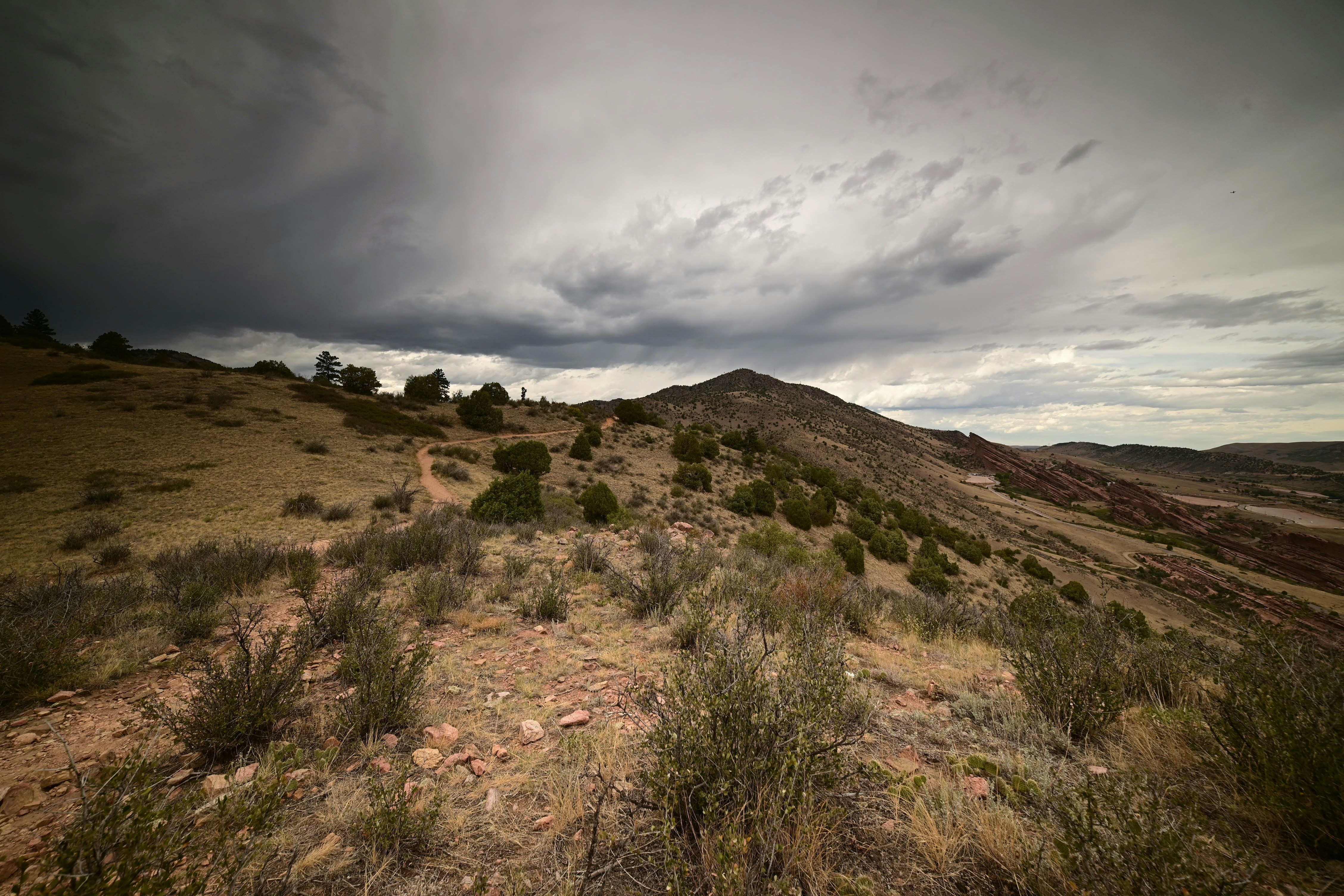 A dirt trail winding through a dry hilly landscape under a dark stormy sky
