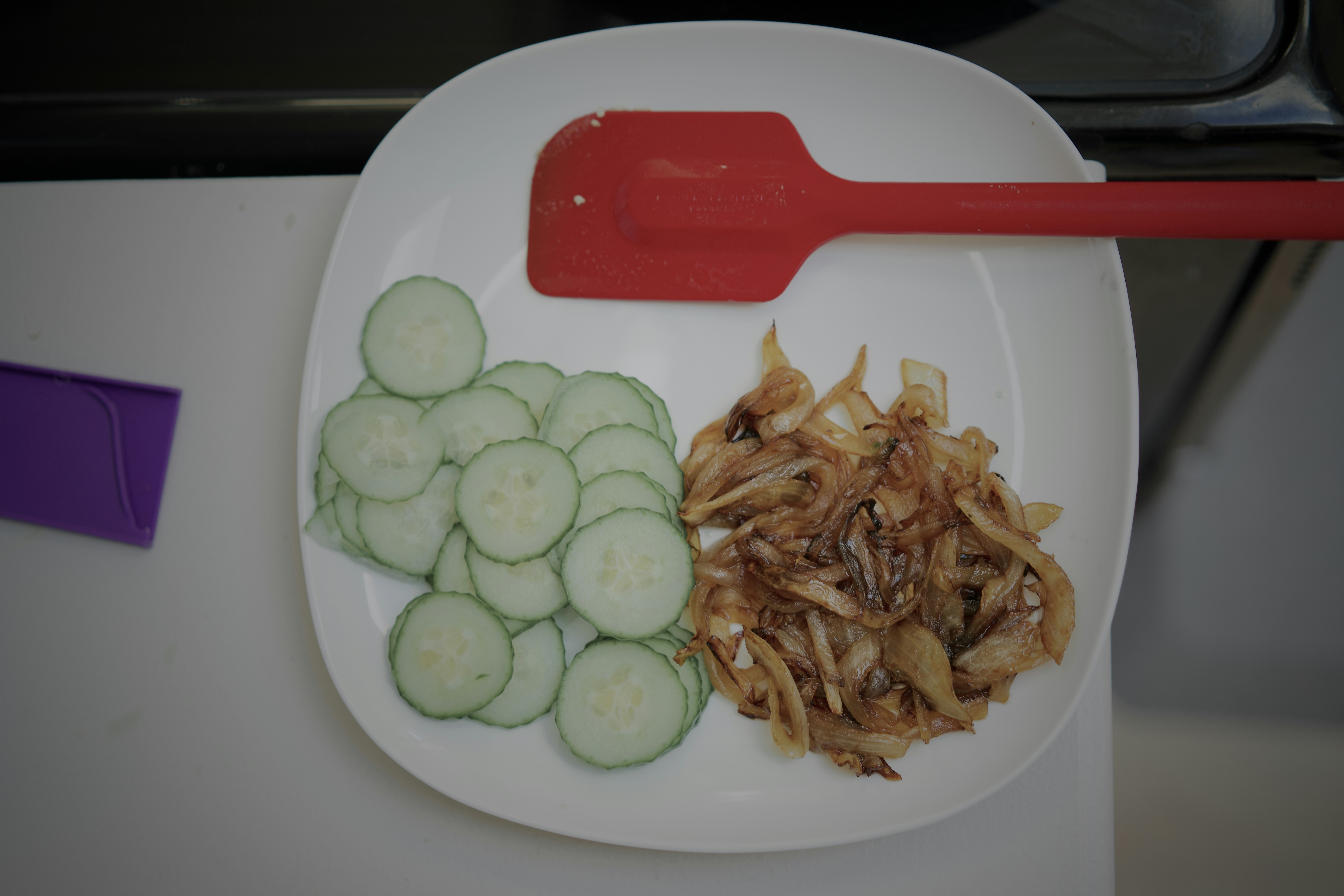 Iris mentimun dan bawang karamel di piring putih dengan spatula merah