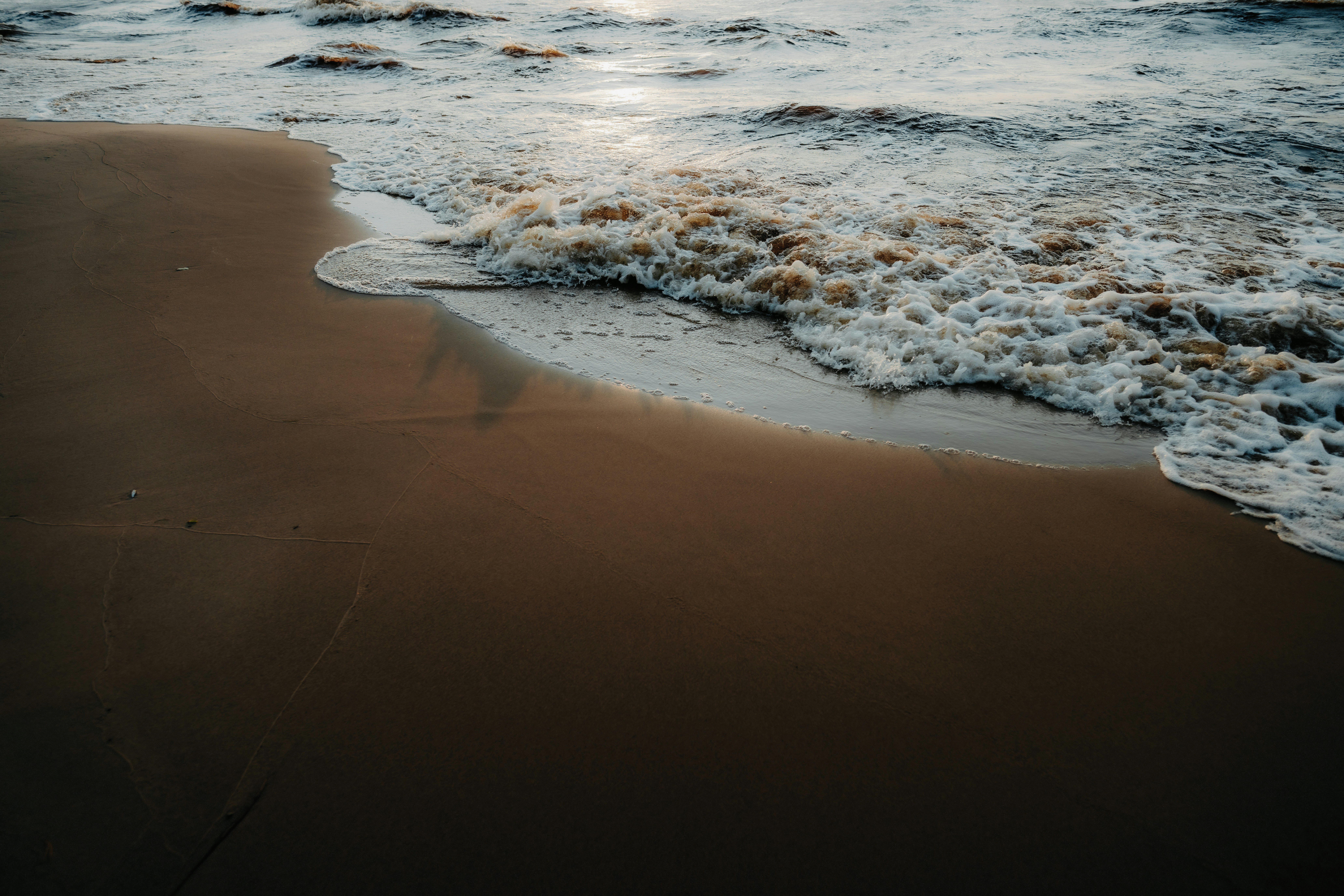 Olas espumosas del océano arrastrándose sobre la arena lisa y húmeda en una playa