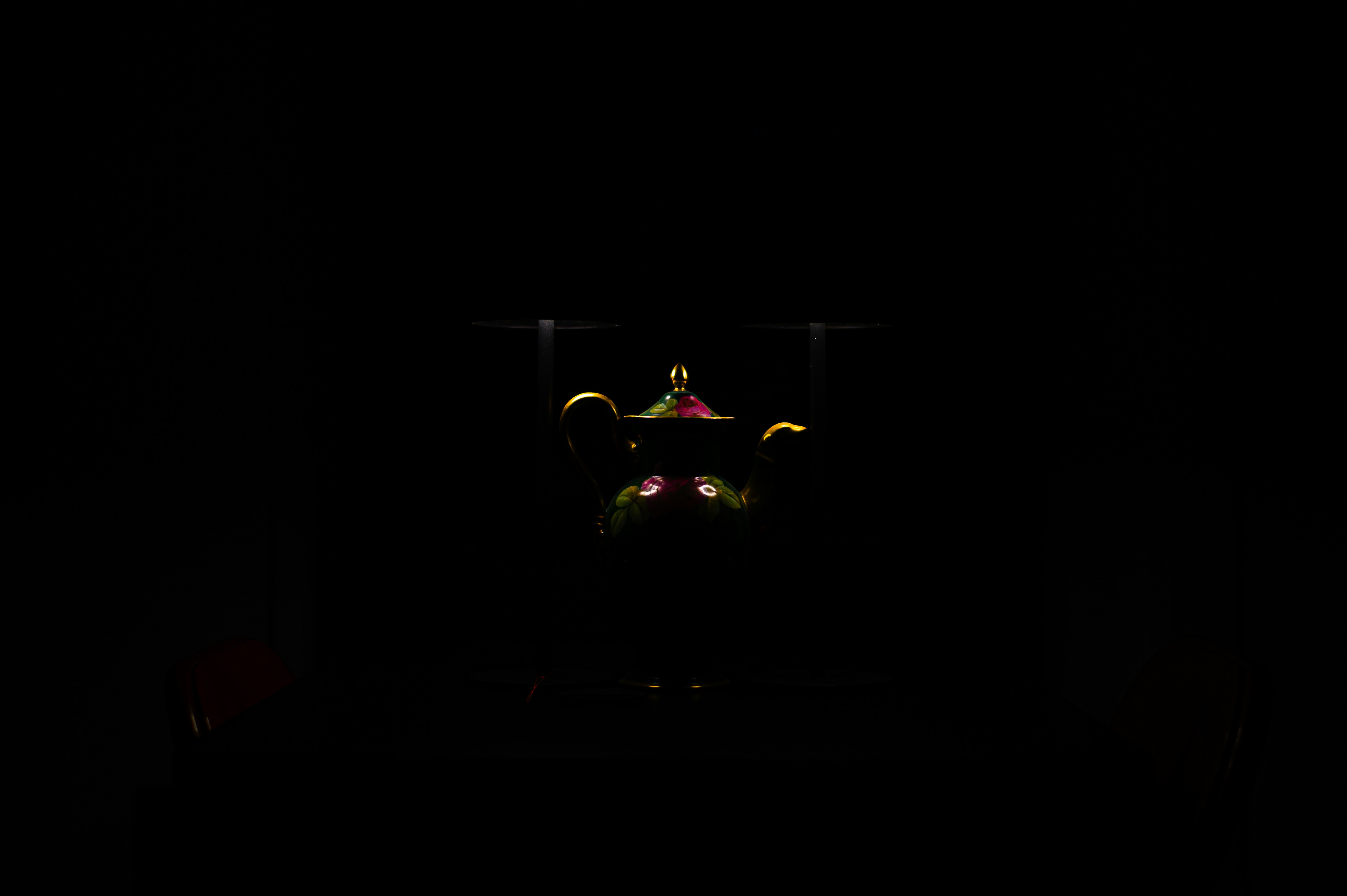 A floral porcelain teapot with gold trim illuminated against a dark background