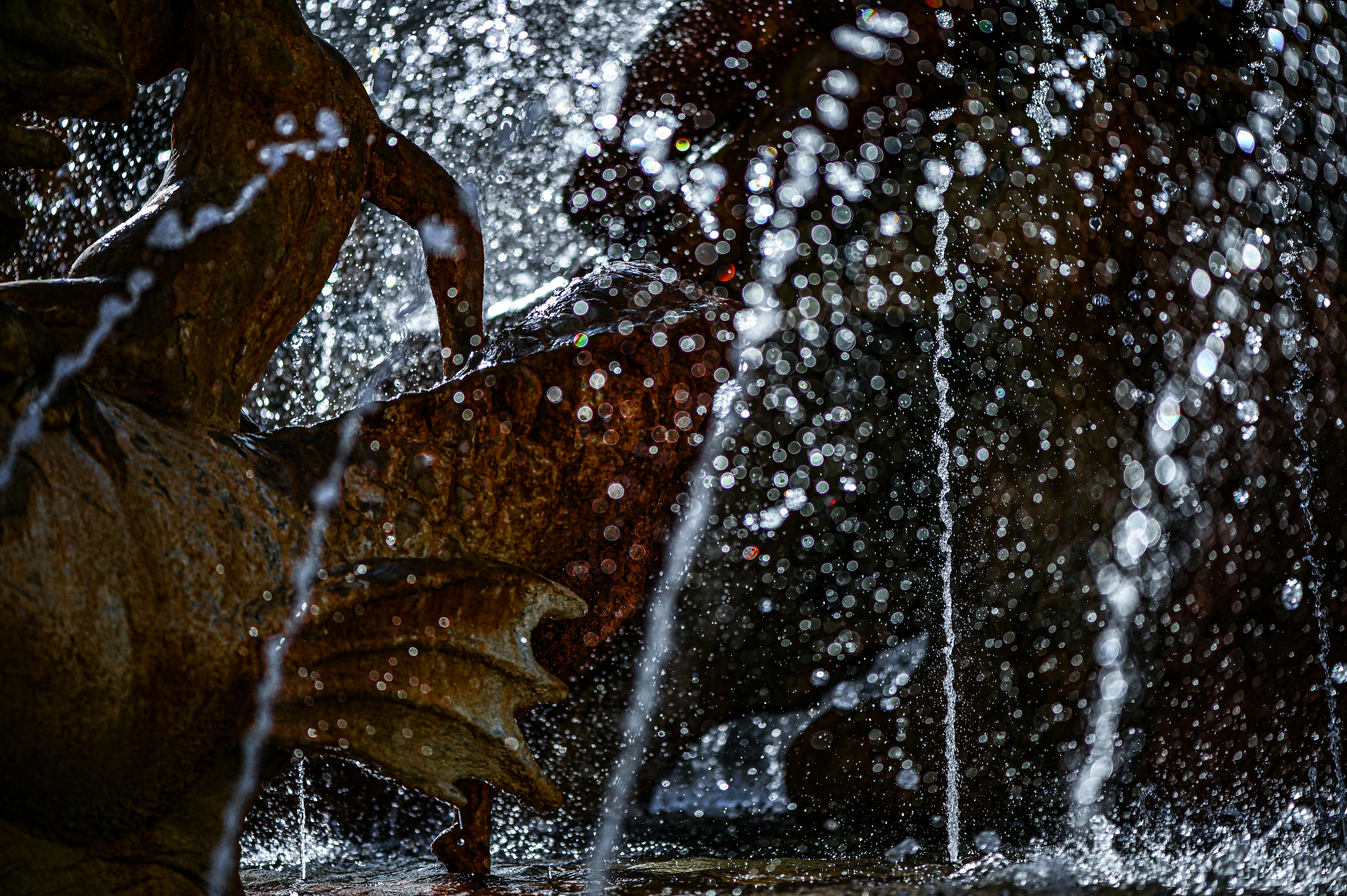 Water droplets spraying from a stone fountain sculpture with bokeh light reflections