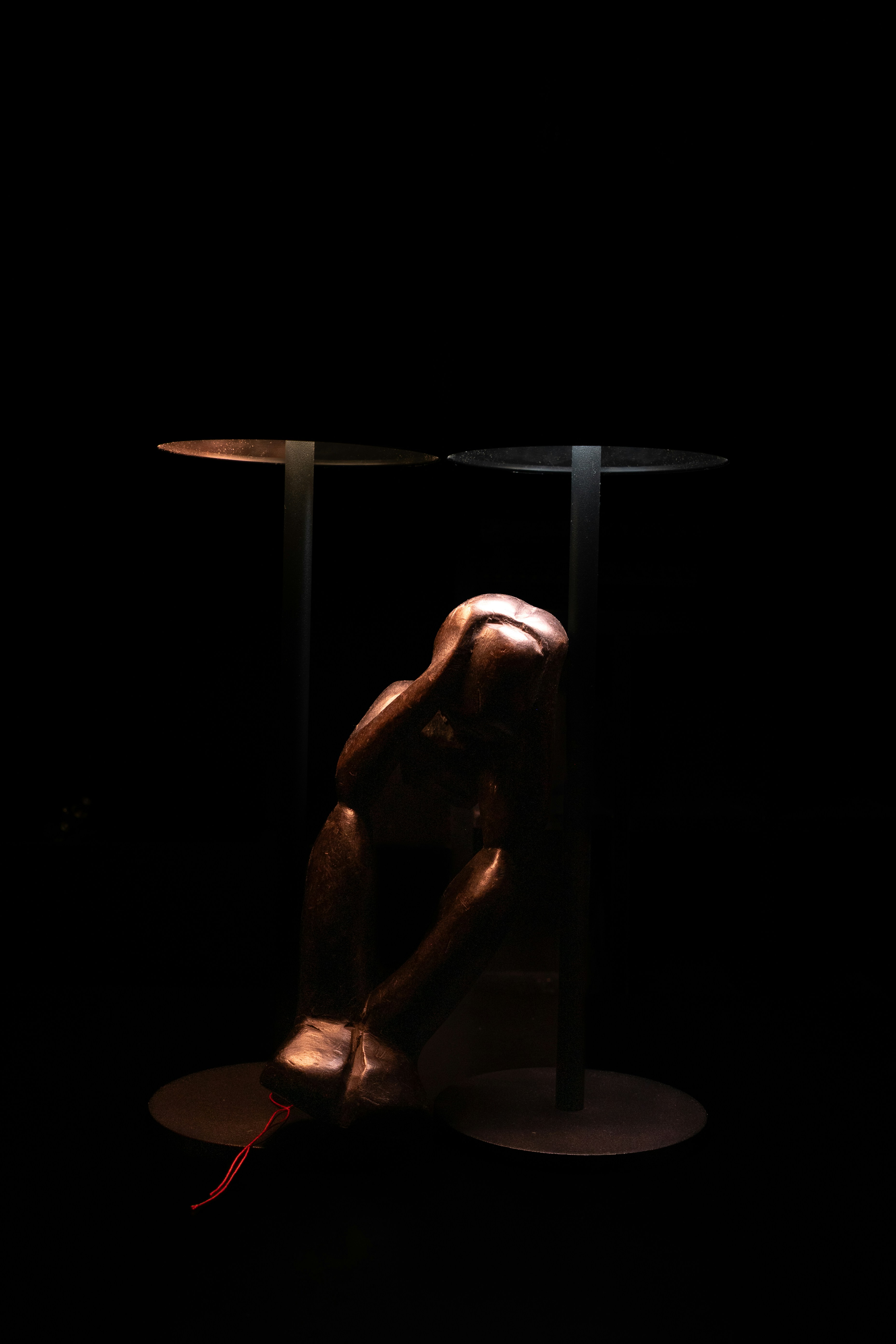 A bronze sculpture of a person with hands on head between two lamps