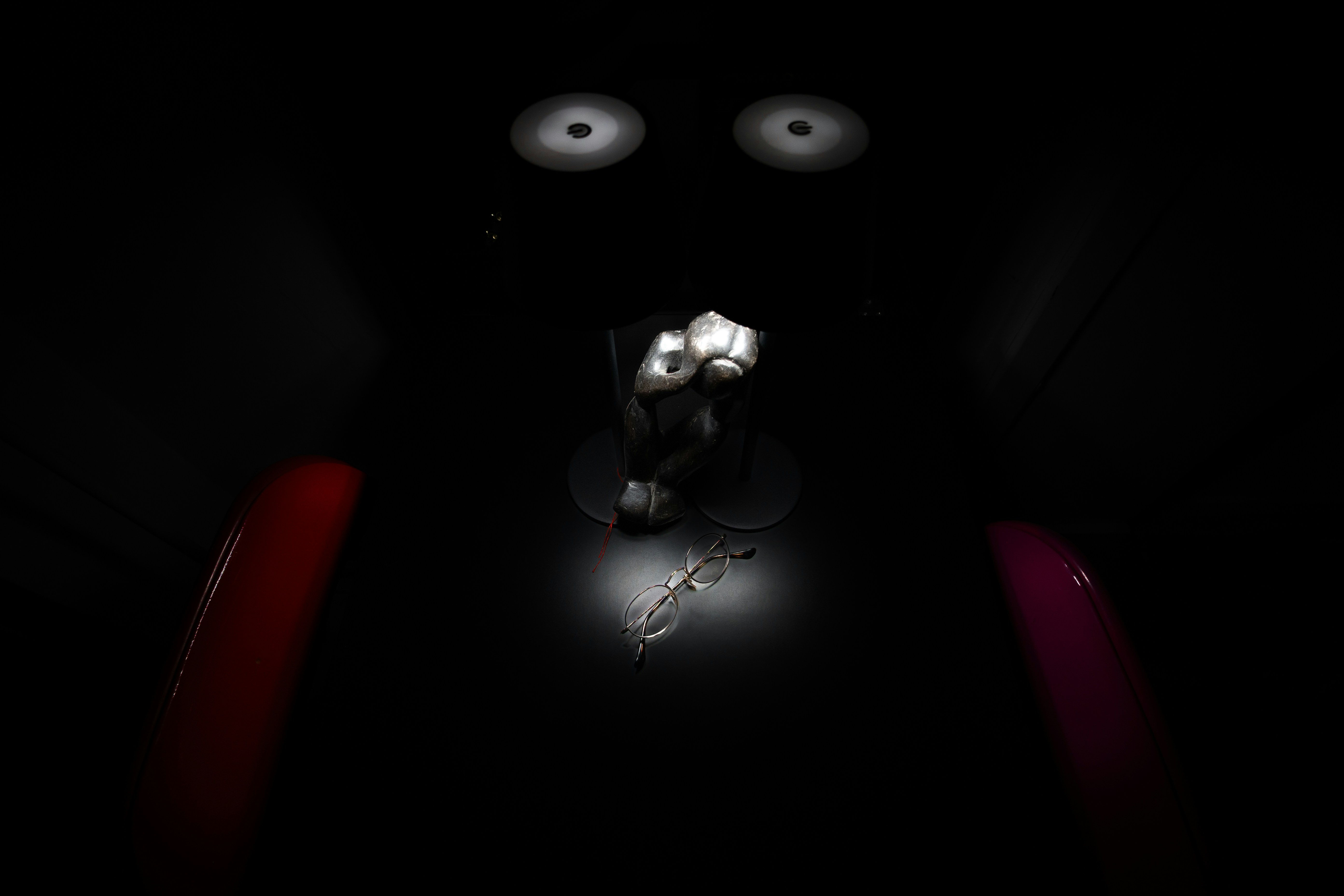 A small metal sculpture and eyeglasses illuminated by a spotlight in a dark room