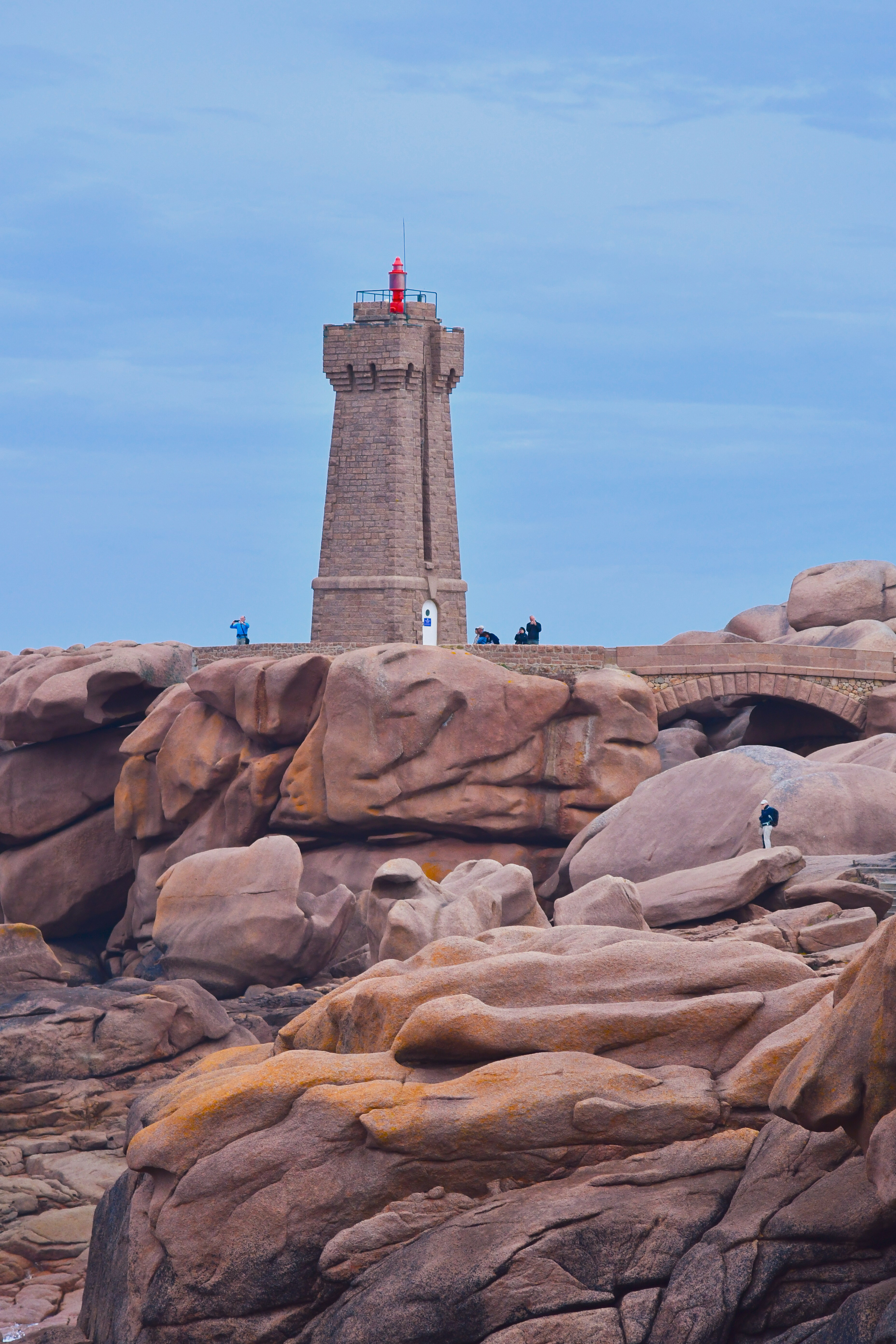 Ein steinerner Leuchtturm an einer felsigen, rosafarbenen Granitküste mit Menschen in der Nähe