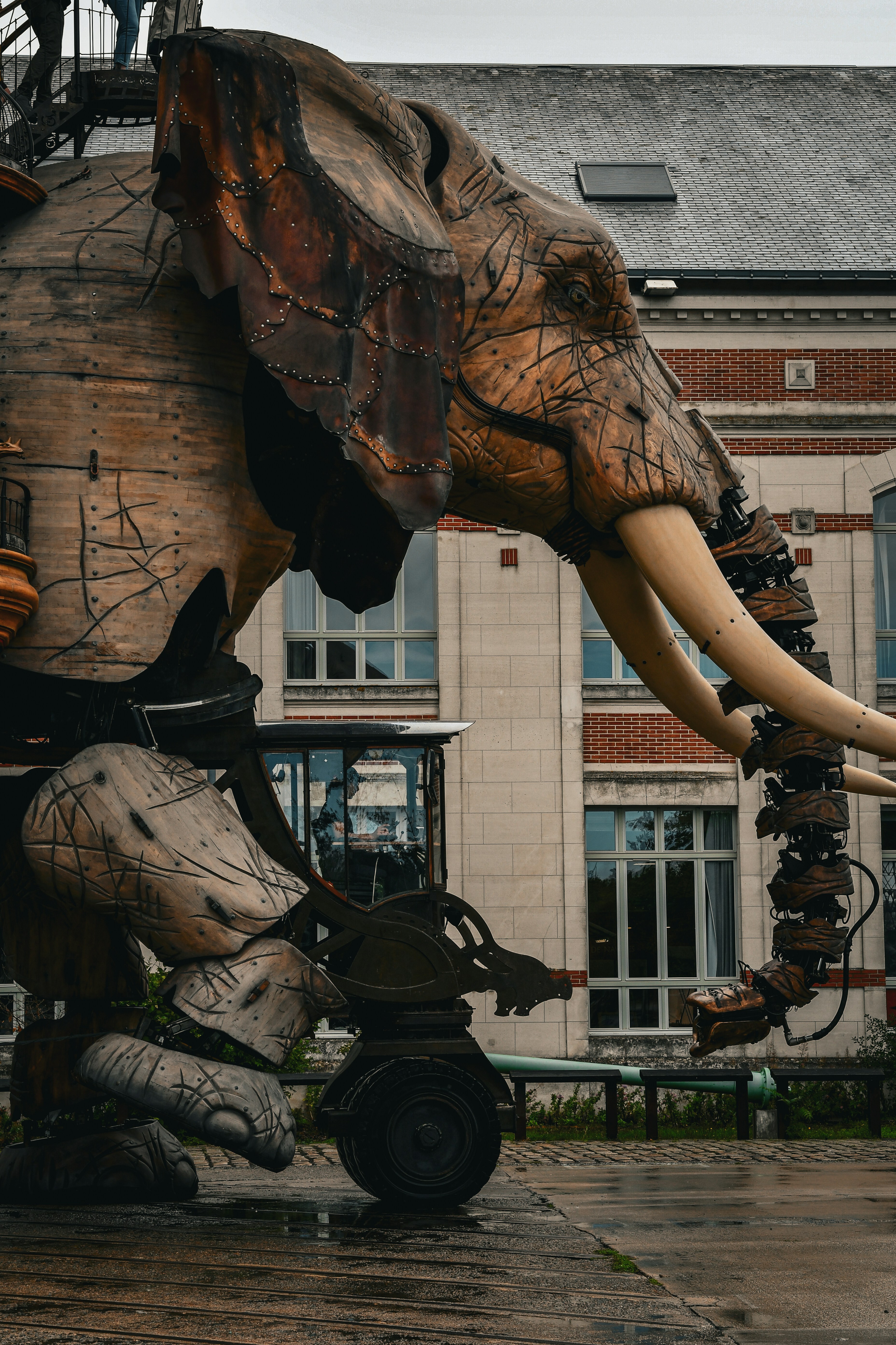 Eine riesige mechanische Elefantenskulptur mit Holzpaneelen und Stoßzähnen vor einem Backsteingebäude