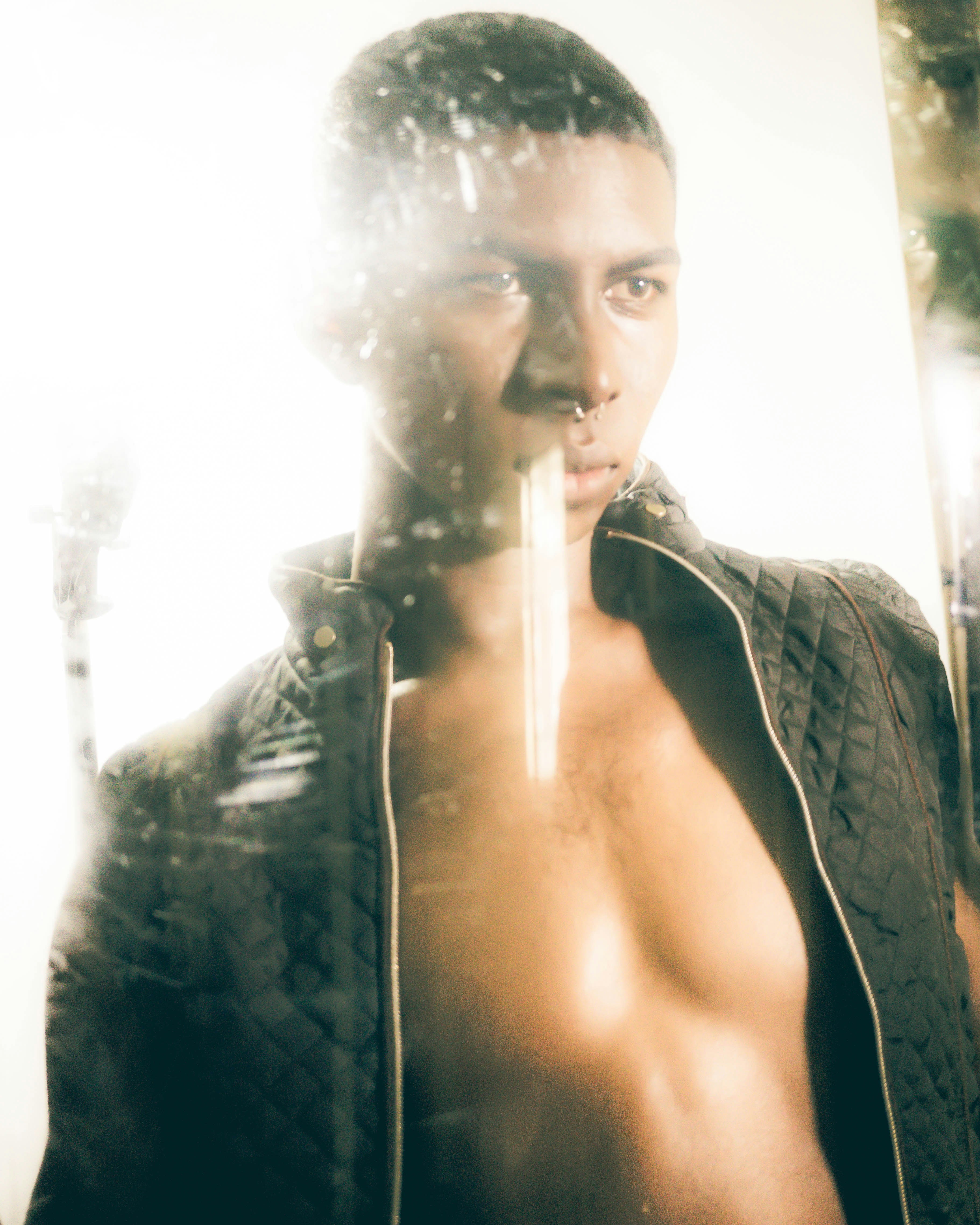 A person in an unzipped quilted jacket behind a reflective glass surface