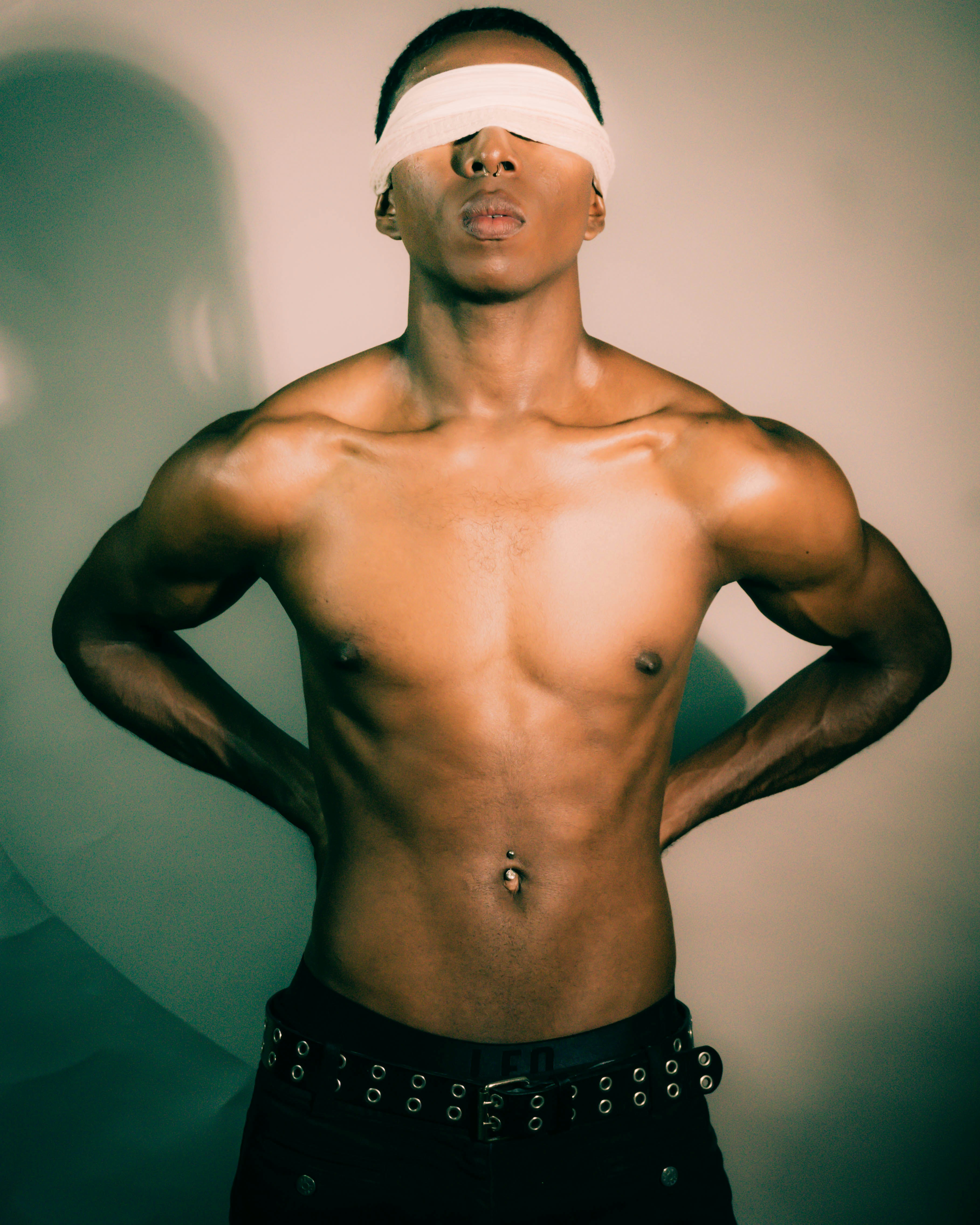 A shirtless man with a white blindfold and a black grommet belt