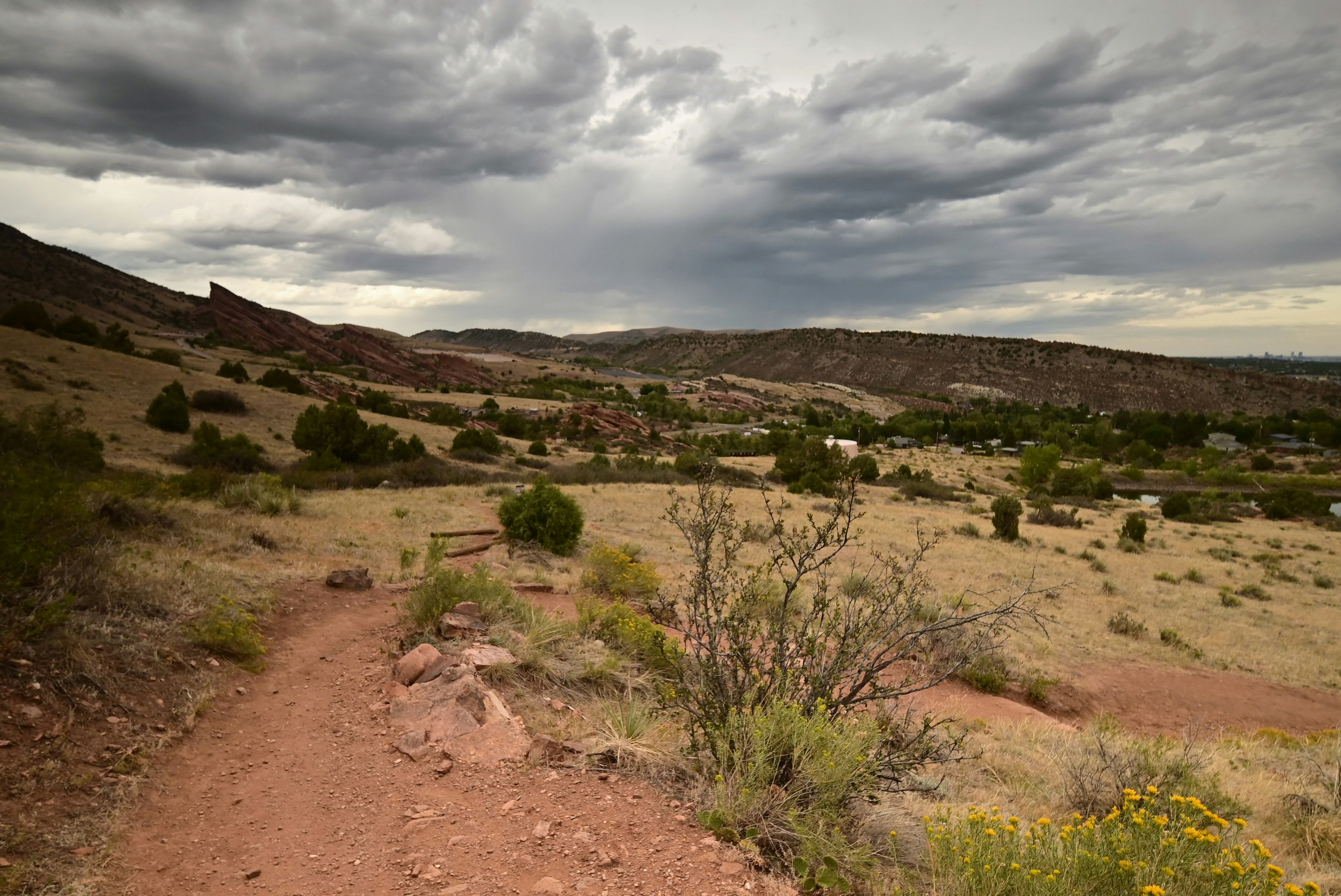 A dirt hiking trail winding through a dry grassy landscape under stormy clouds