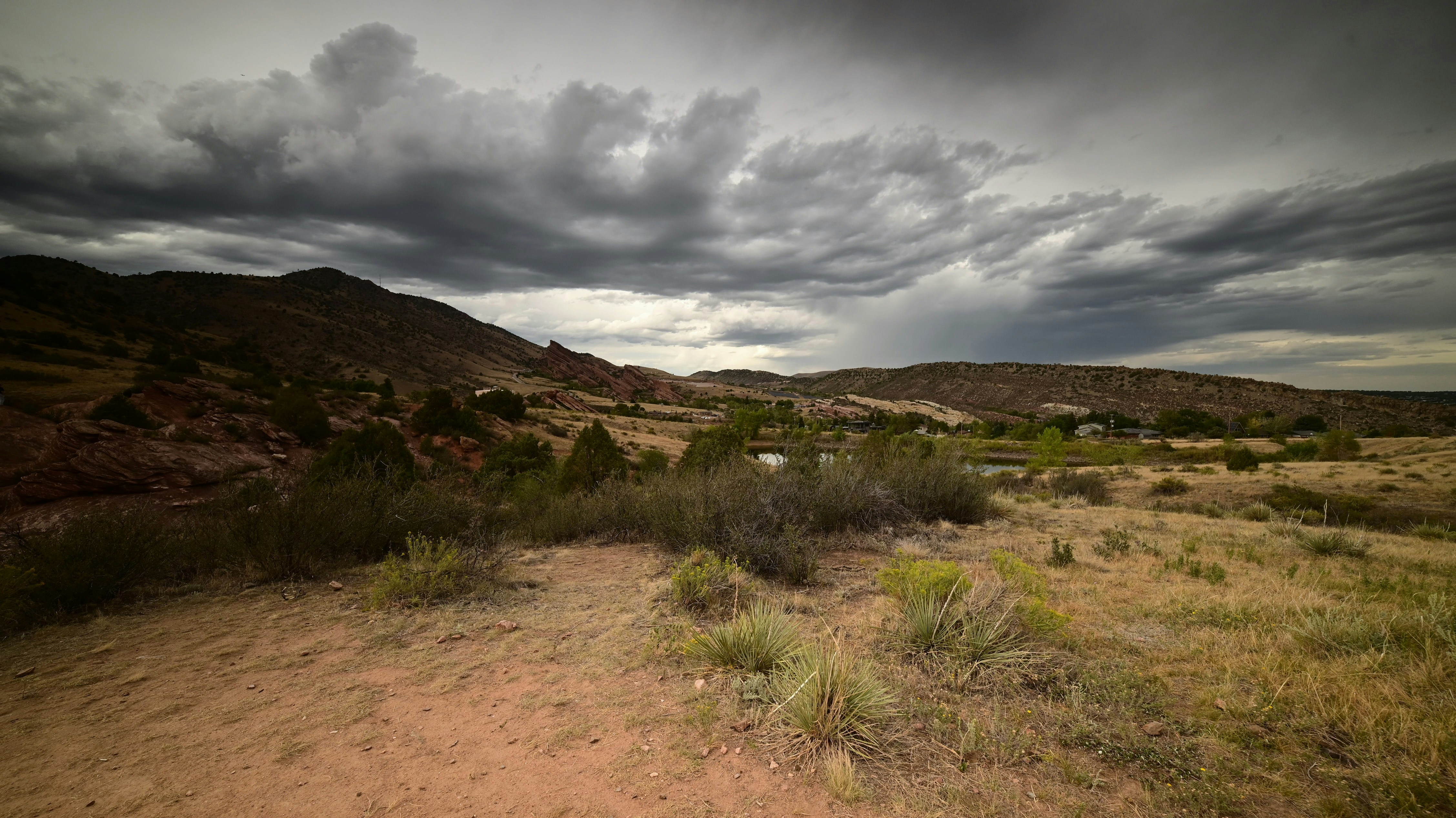 A dry landscape with red rock formations under a heavy, dark, cloudy sky