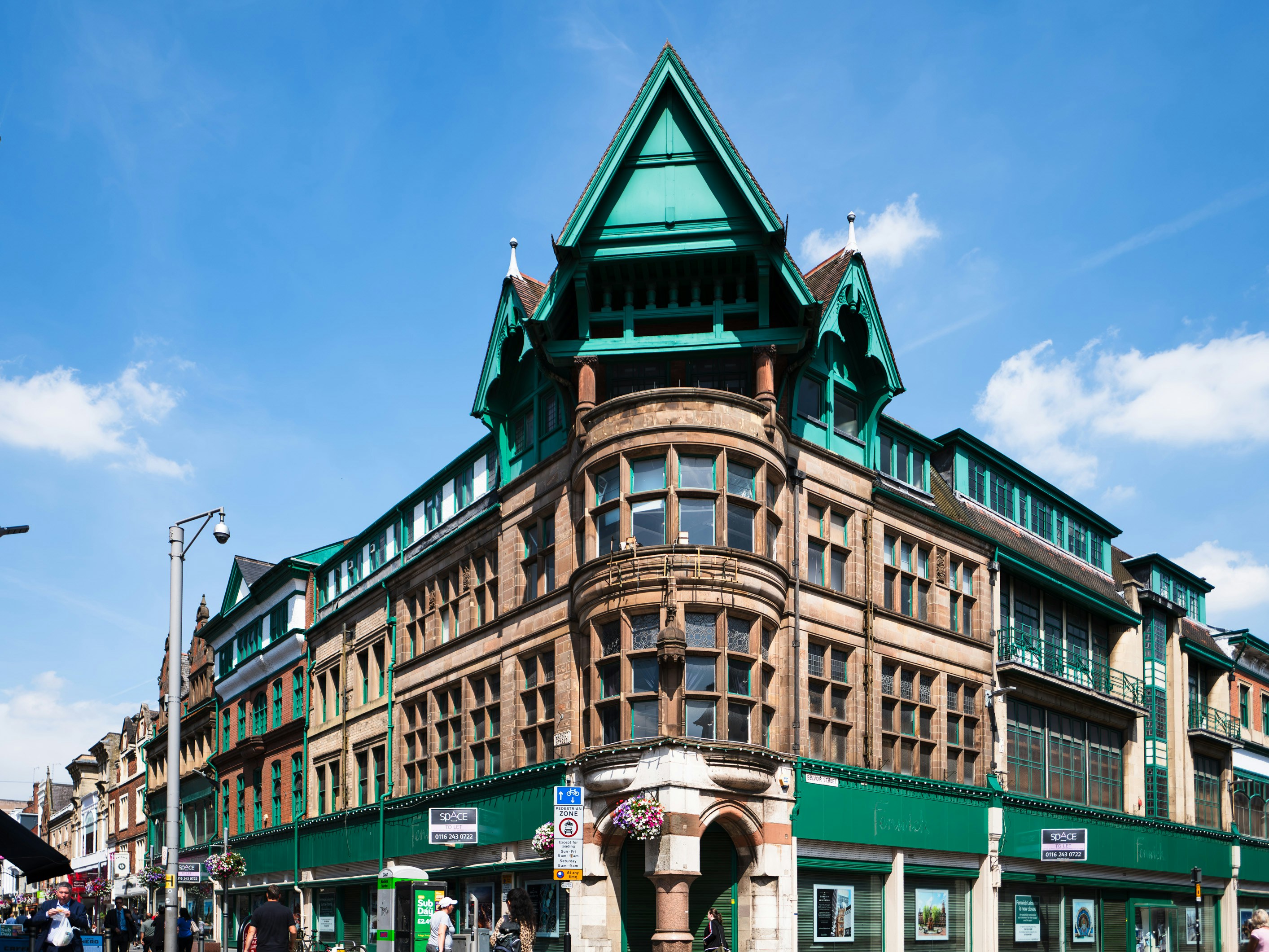 An ornate stone and green timber building on a sunny city street corner