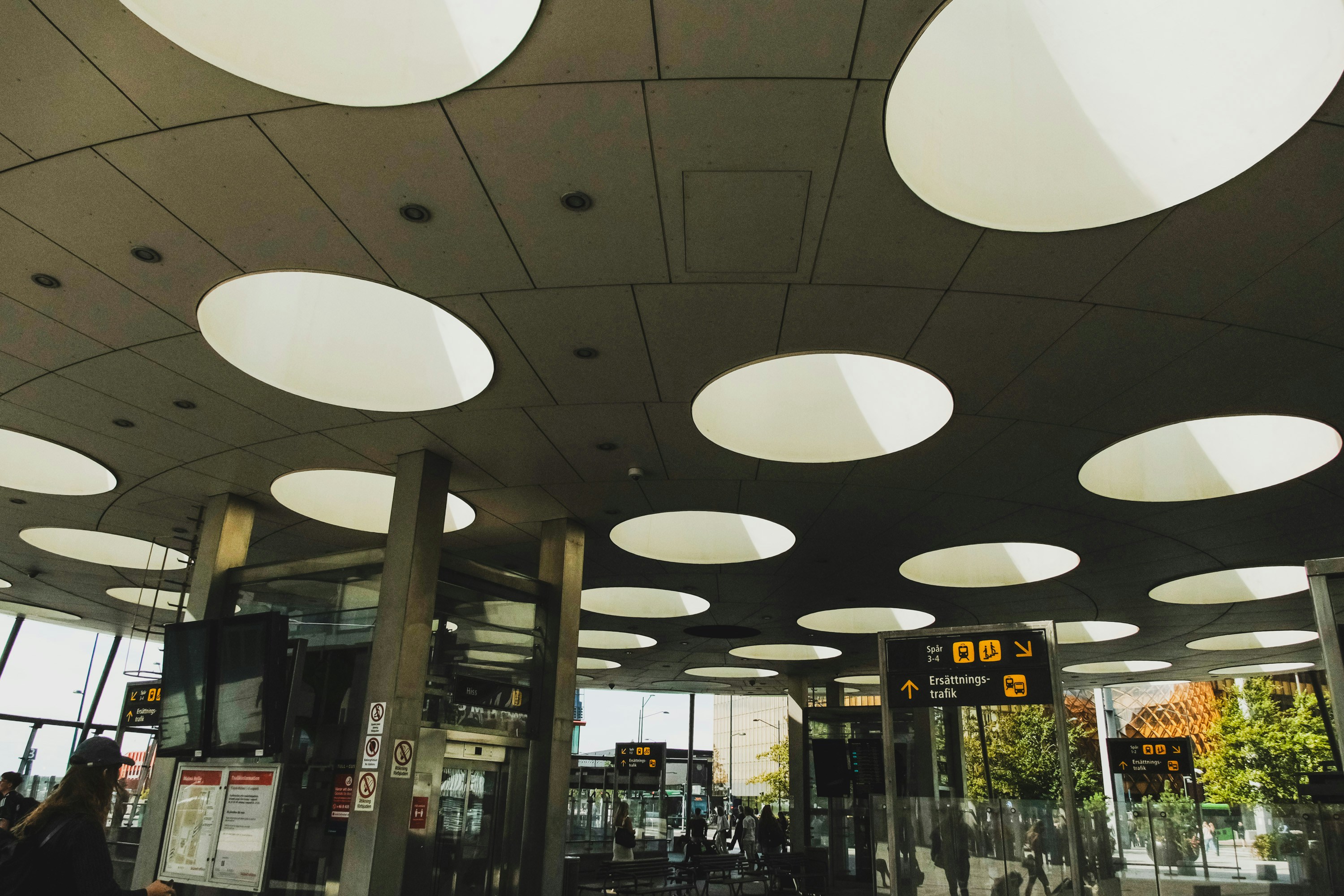 A modern transit station ceiling with circular skylights and yellow directional signage