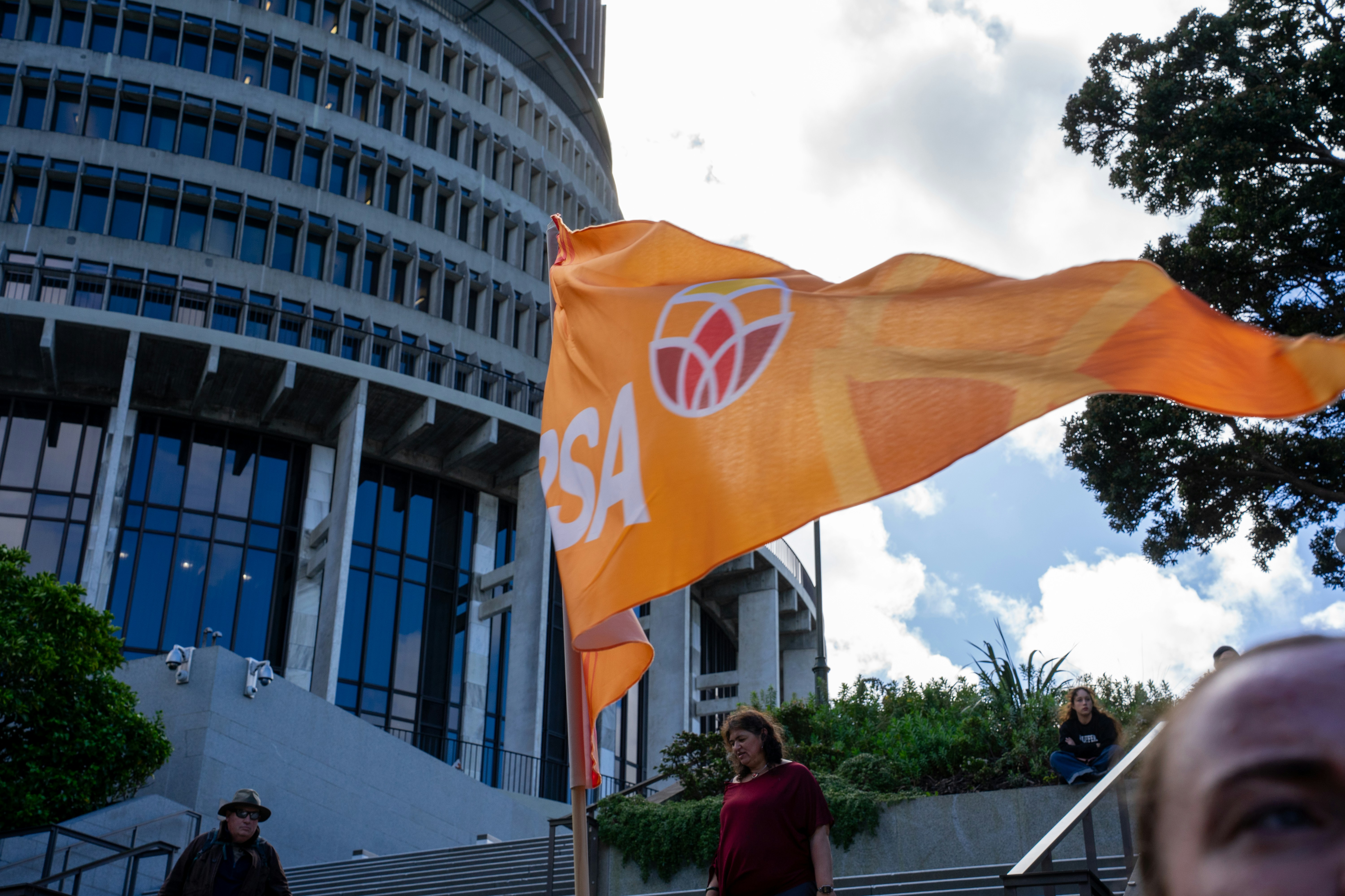 Un drapeau orange avec un logo flottant devant le bâtiment Beehive à Wellington