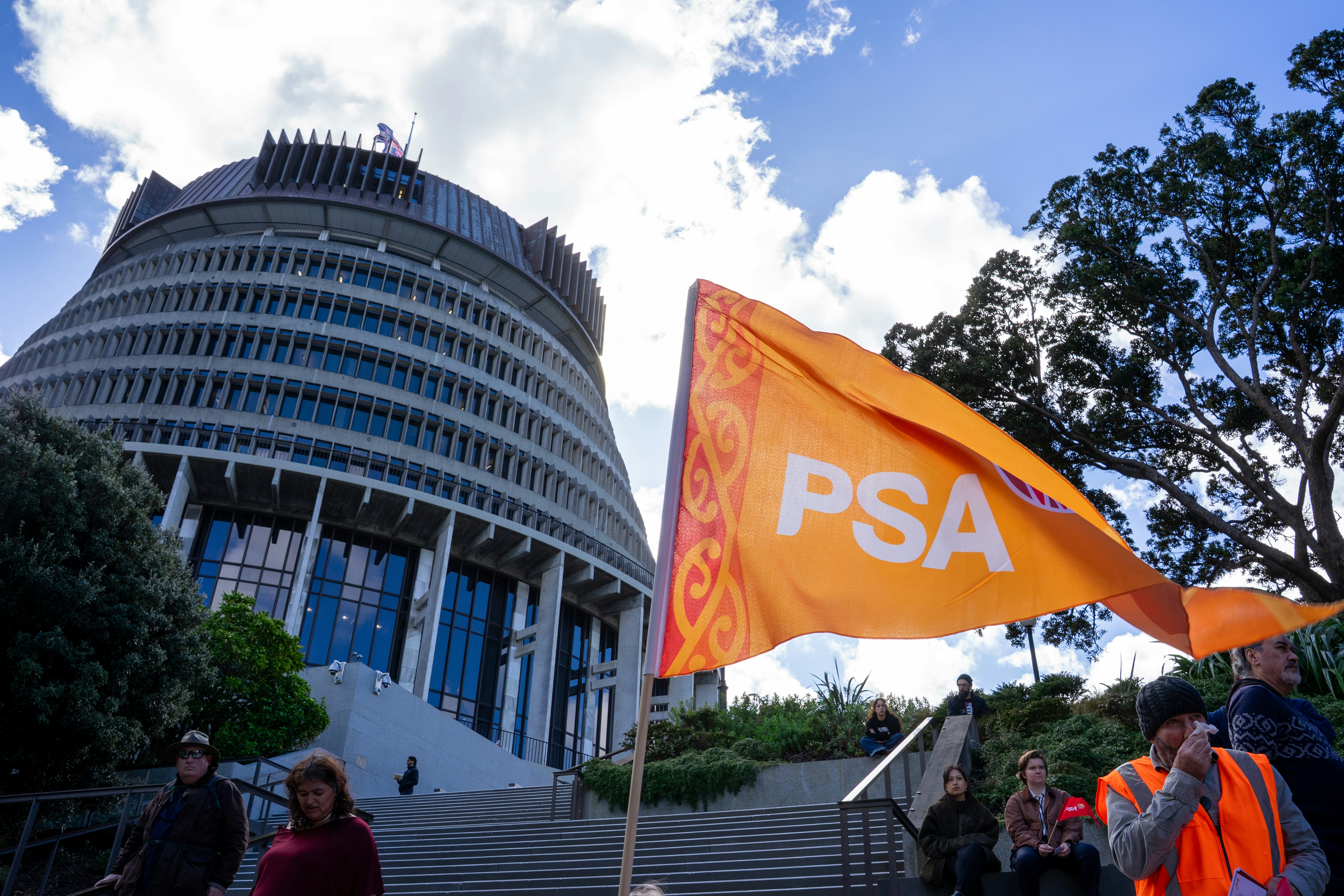 People on steps before the Beehive building in Wellington with an orange PSA flag