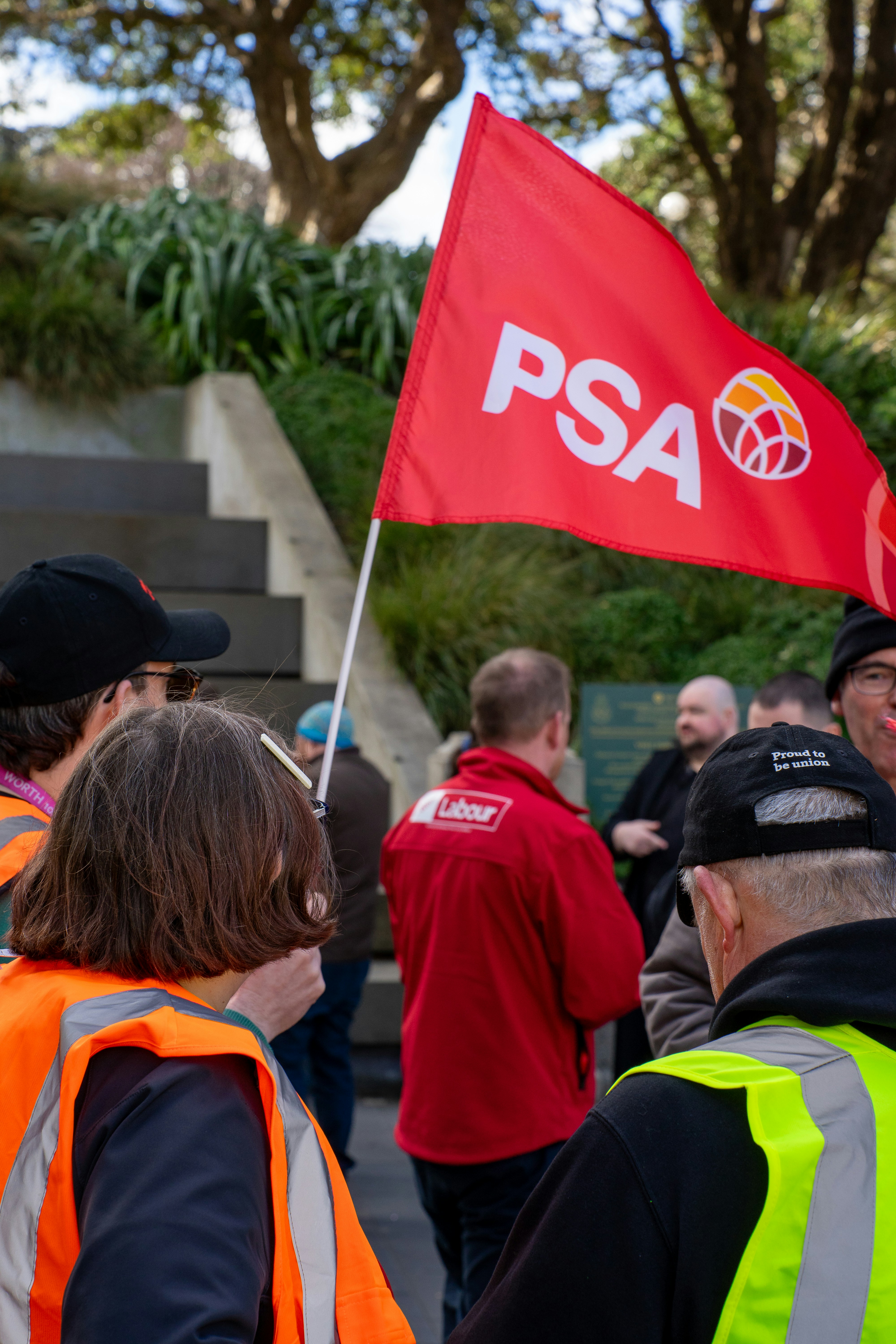 Des personnes en gilets haute visibilité tenant un drapeau rouge de la PSA lors d’un rassemblement en plein air