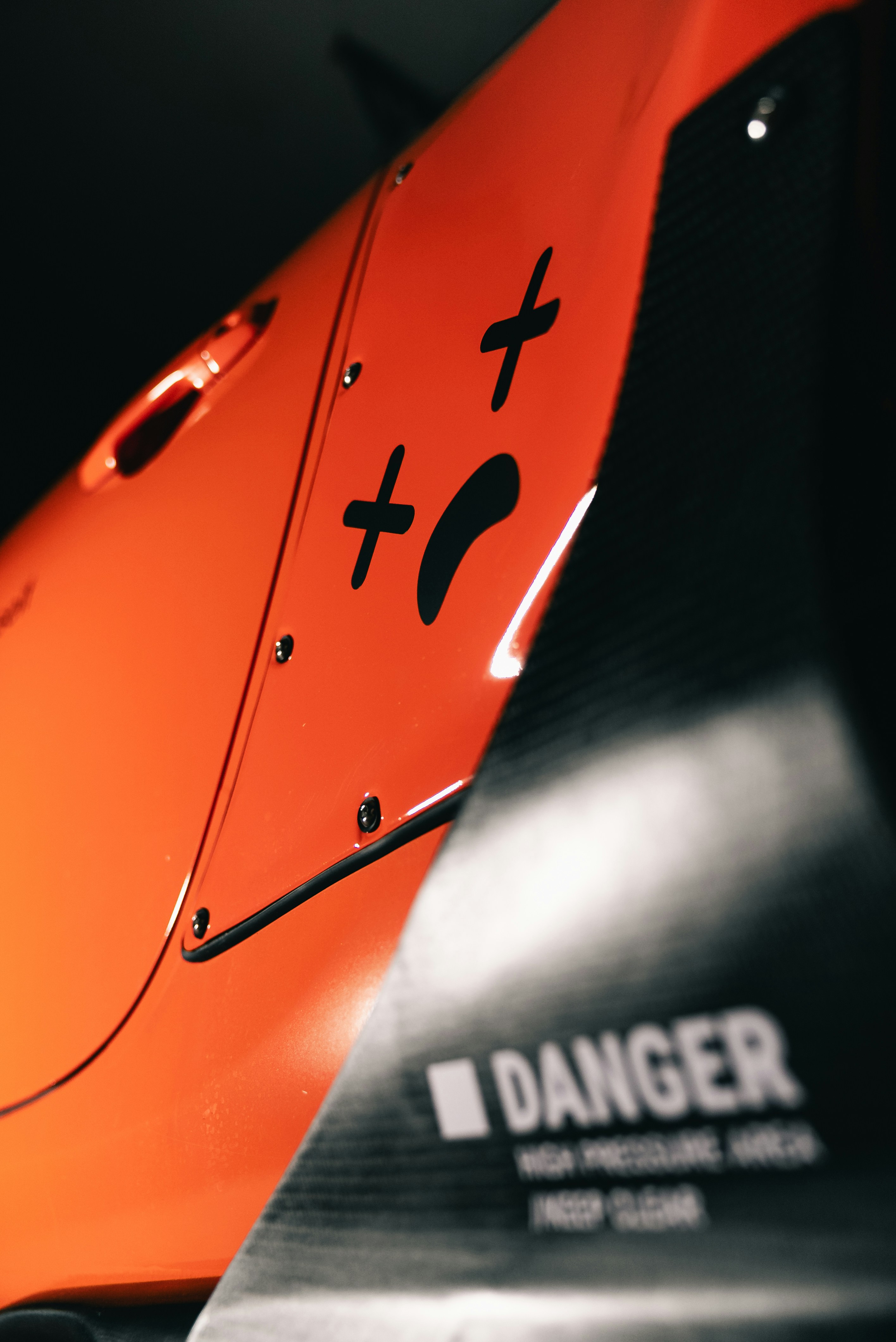 An orange car panel with a black sad face decal and danger warning