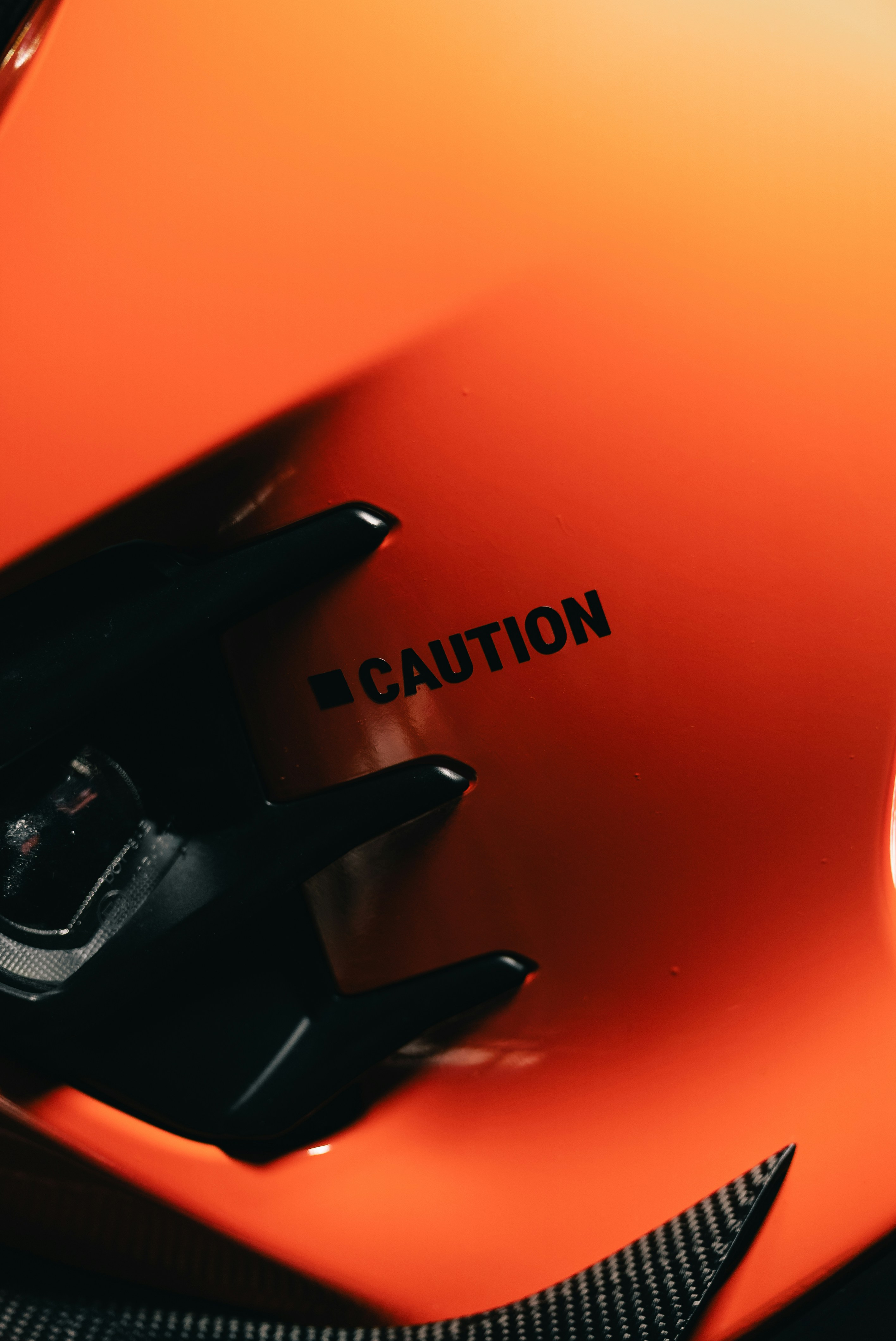 A black caution sign on a glossy orange surface with black plastic components