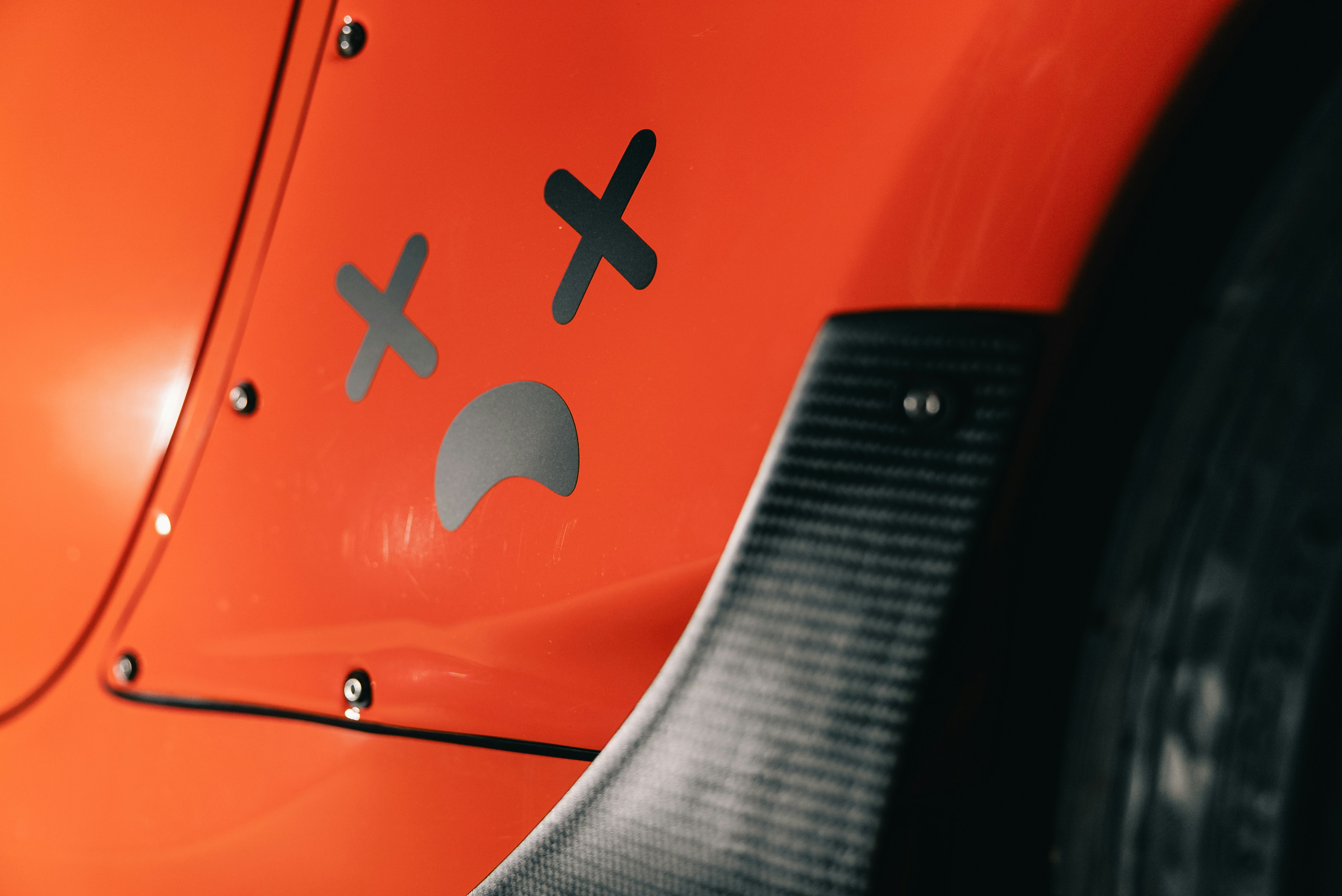 A black sad face decal with x-shaped eyes on an orange car panel