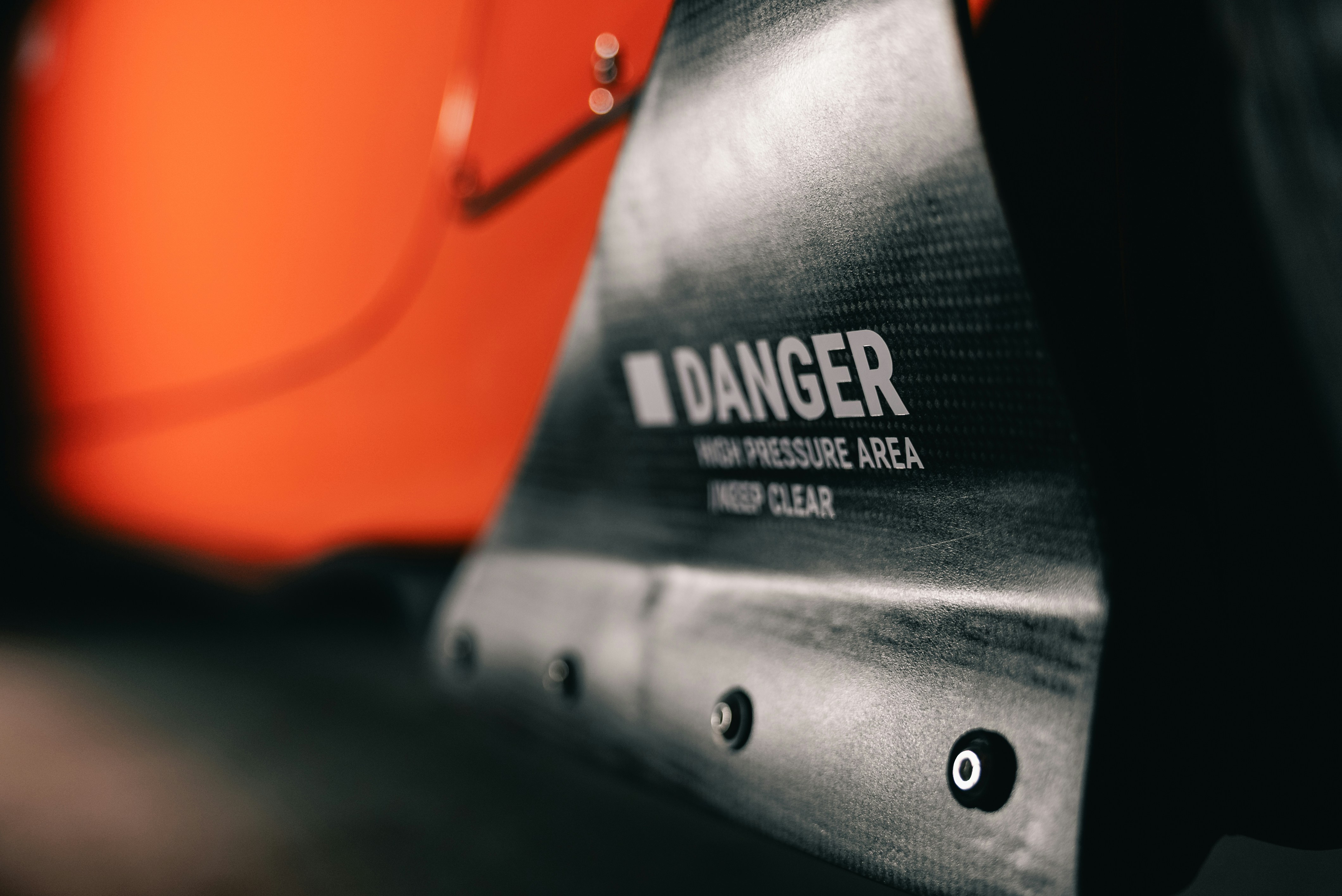 A carbon fiber panel with a DANGER warning label against an orange background