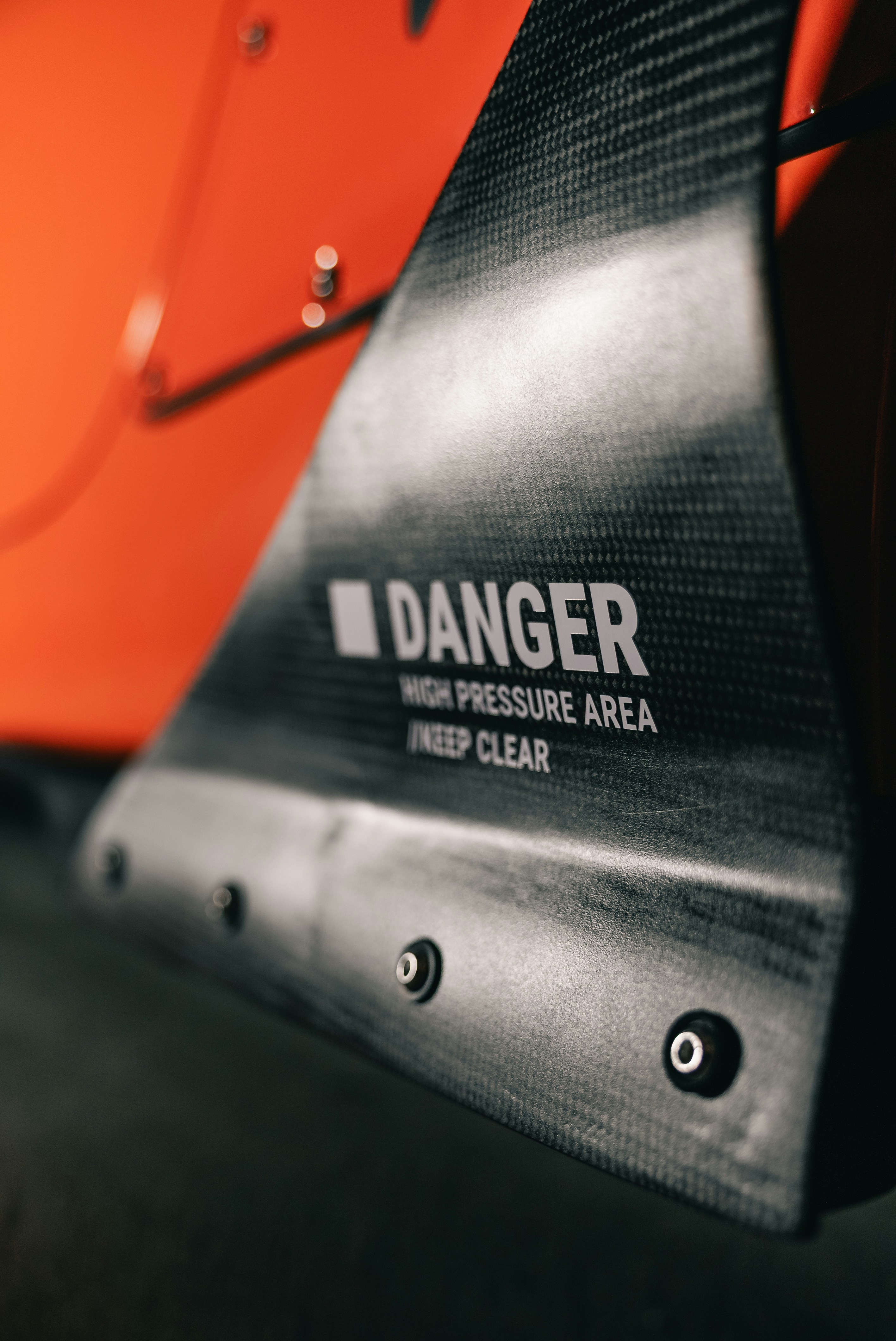 A carbon fiber panel with a warning sign reading DANGER HIGH PRESSURE AREA KEEP CLEAR