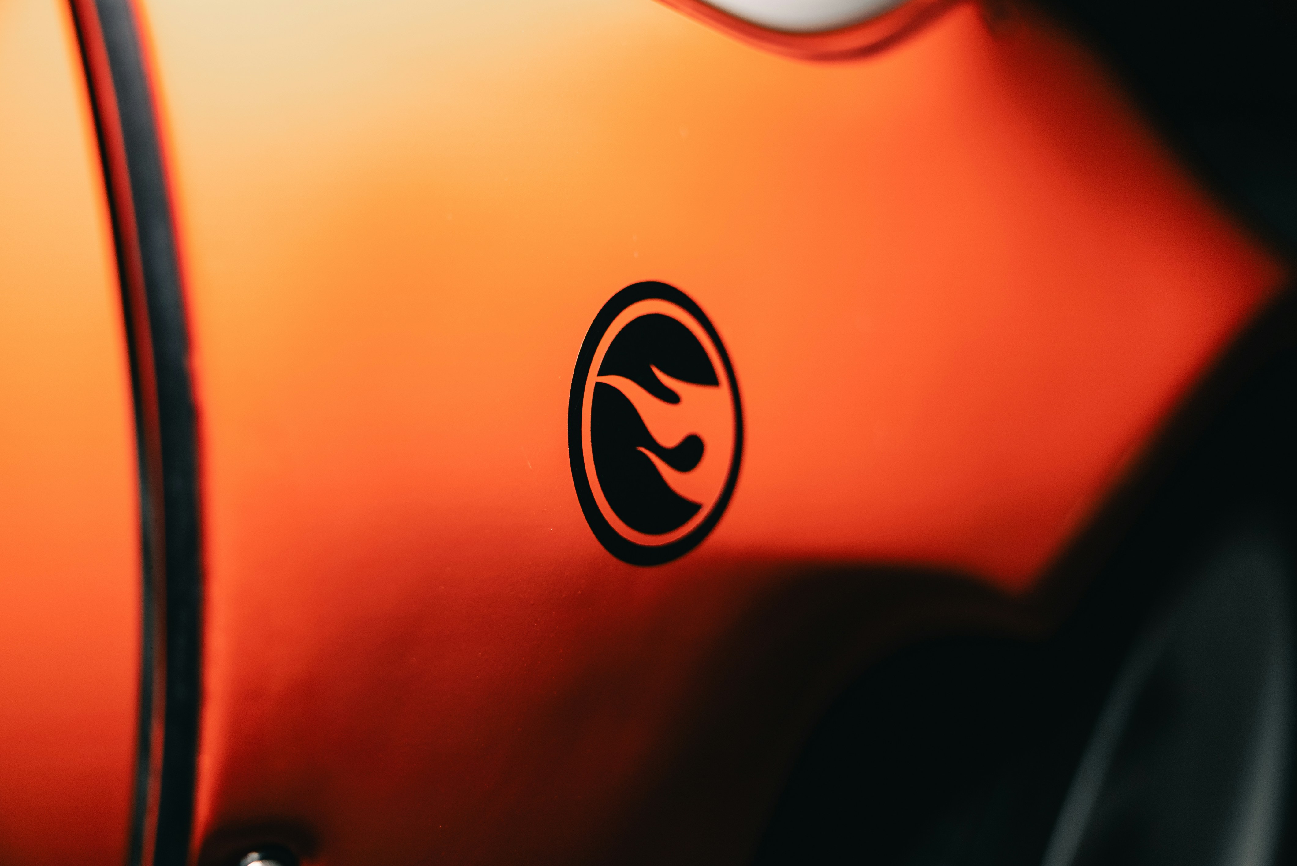 A black flame logo on a smooth orange surface