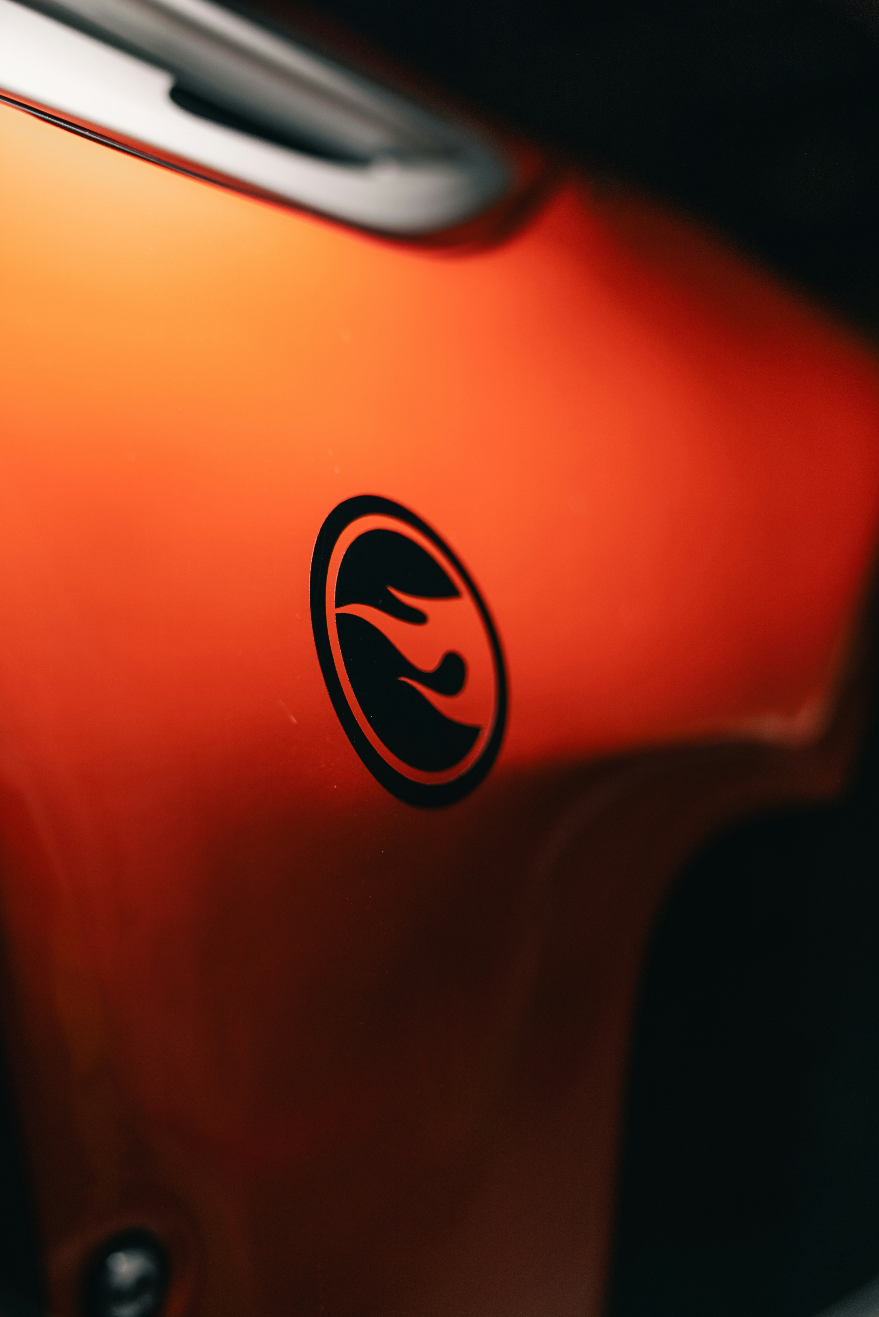 A black flame logo on a smooth orange surface with a metallic edge