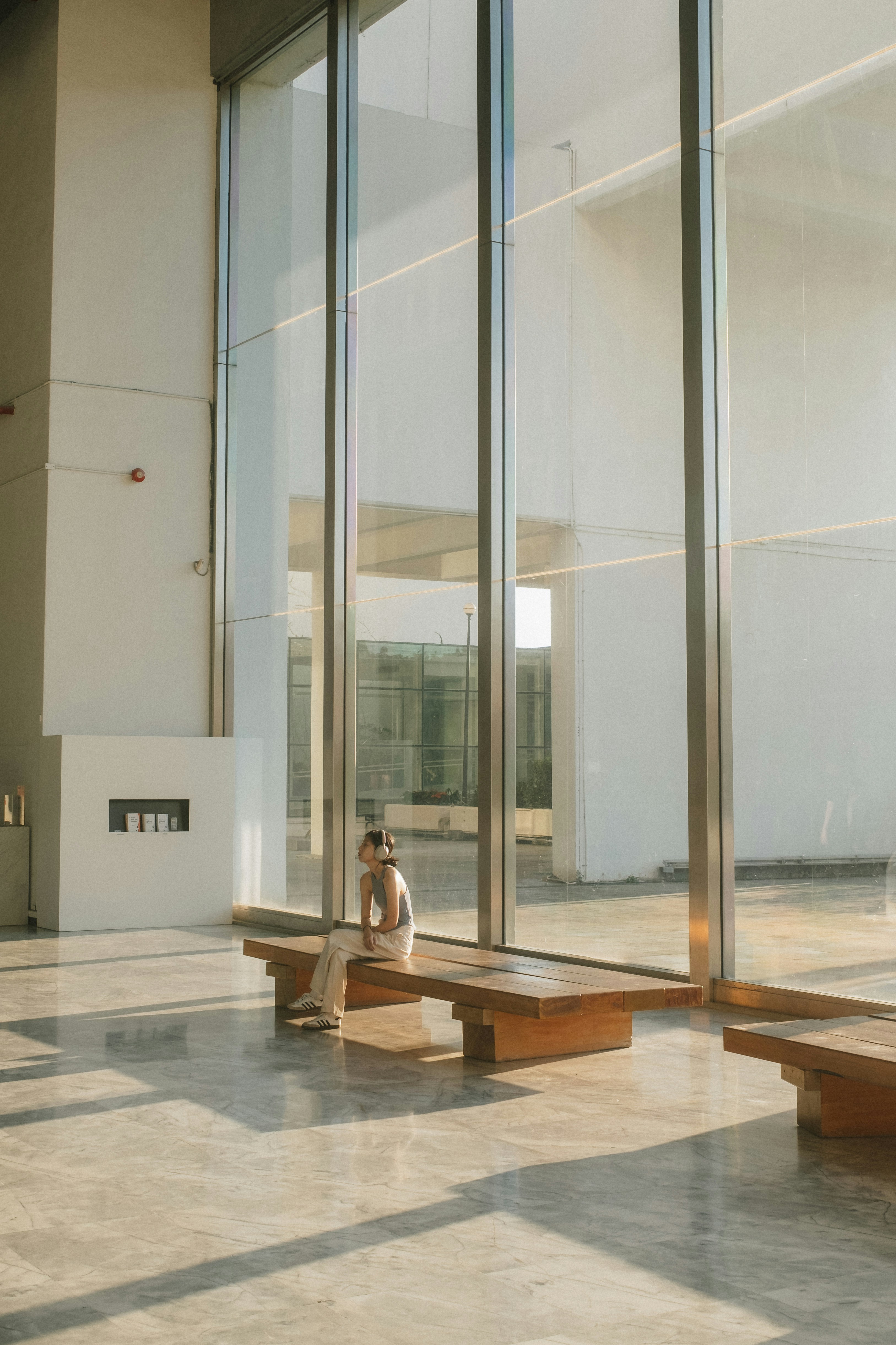 A person wearing headphones on a wooden bench in a sunlit modern lobby