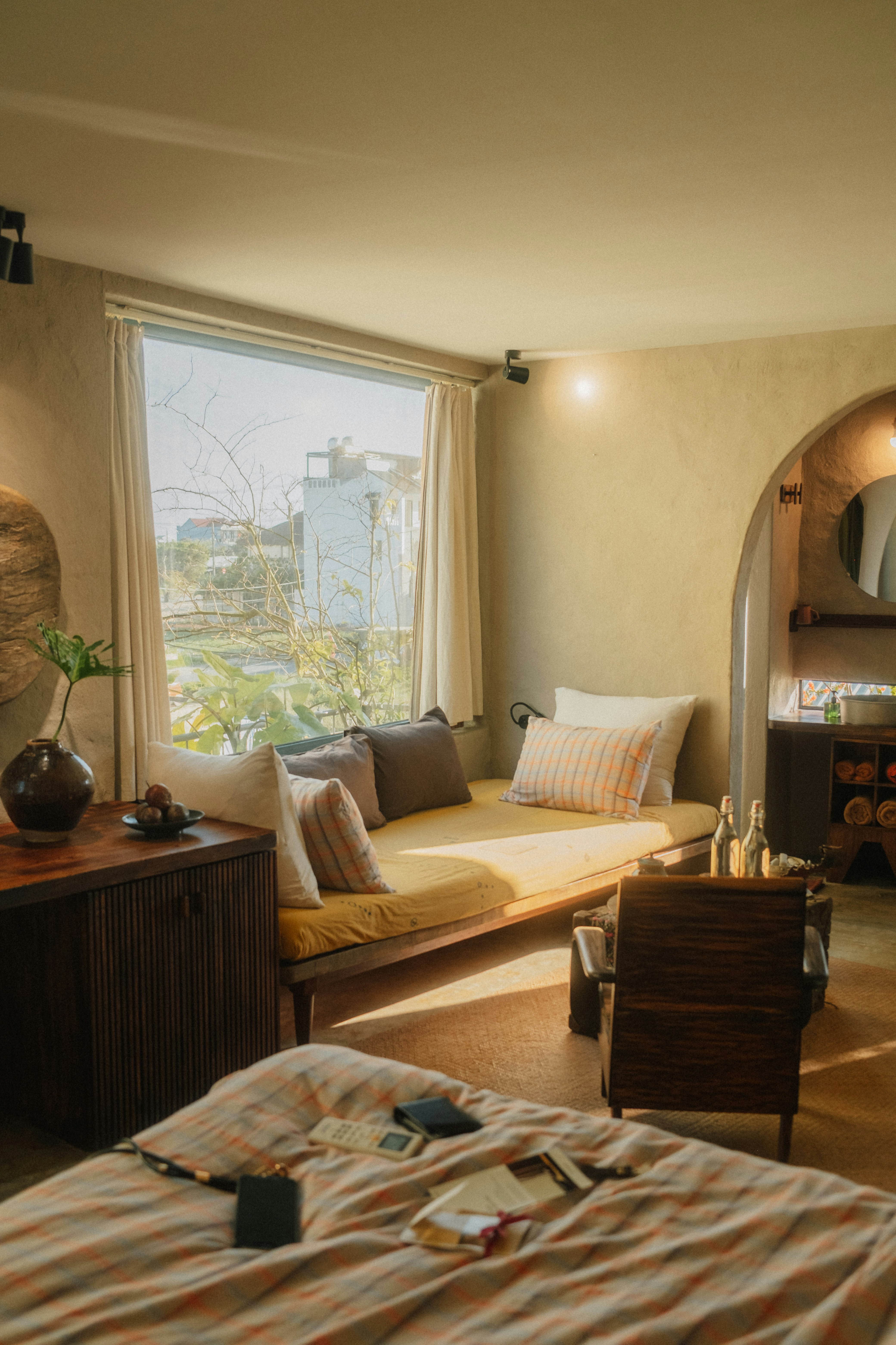 A sunlit bedroom with a daybed, wooden furniture, and a large window view