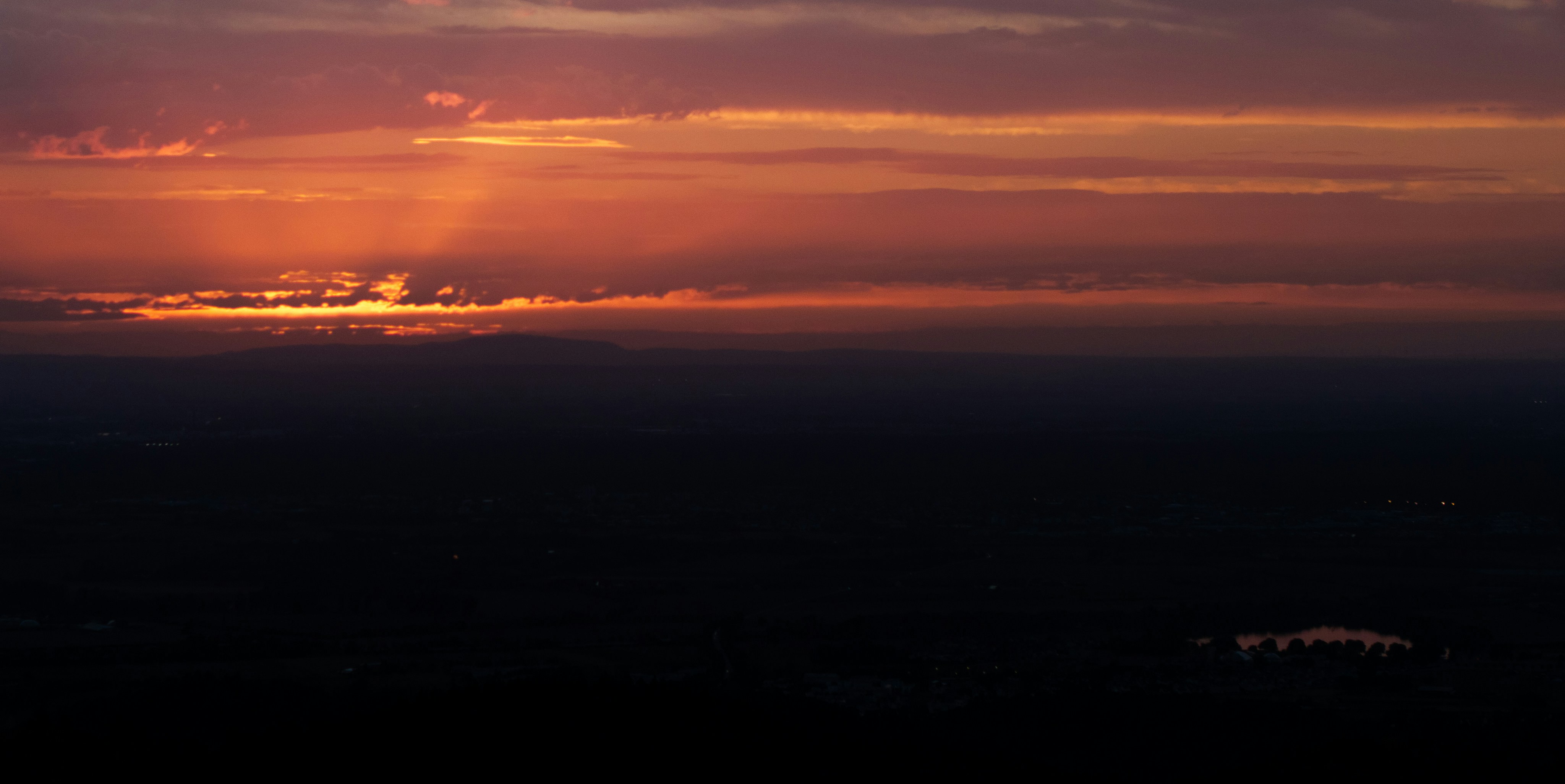 A dark landscape under a vibrant orange and purple sky with low light
