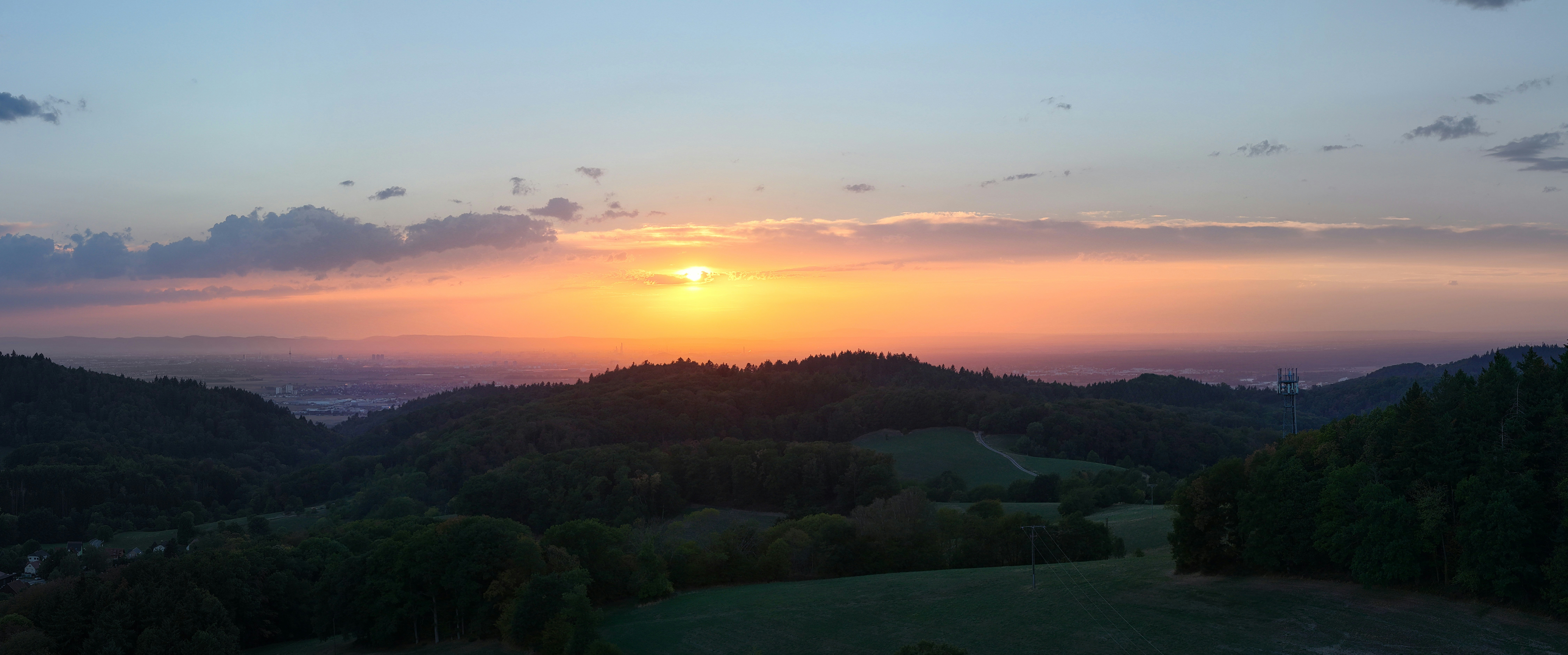 Low sun over a forested valley with distant plains under a warm orange sky