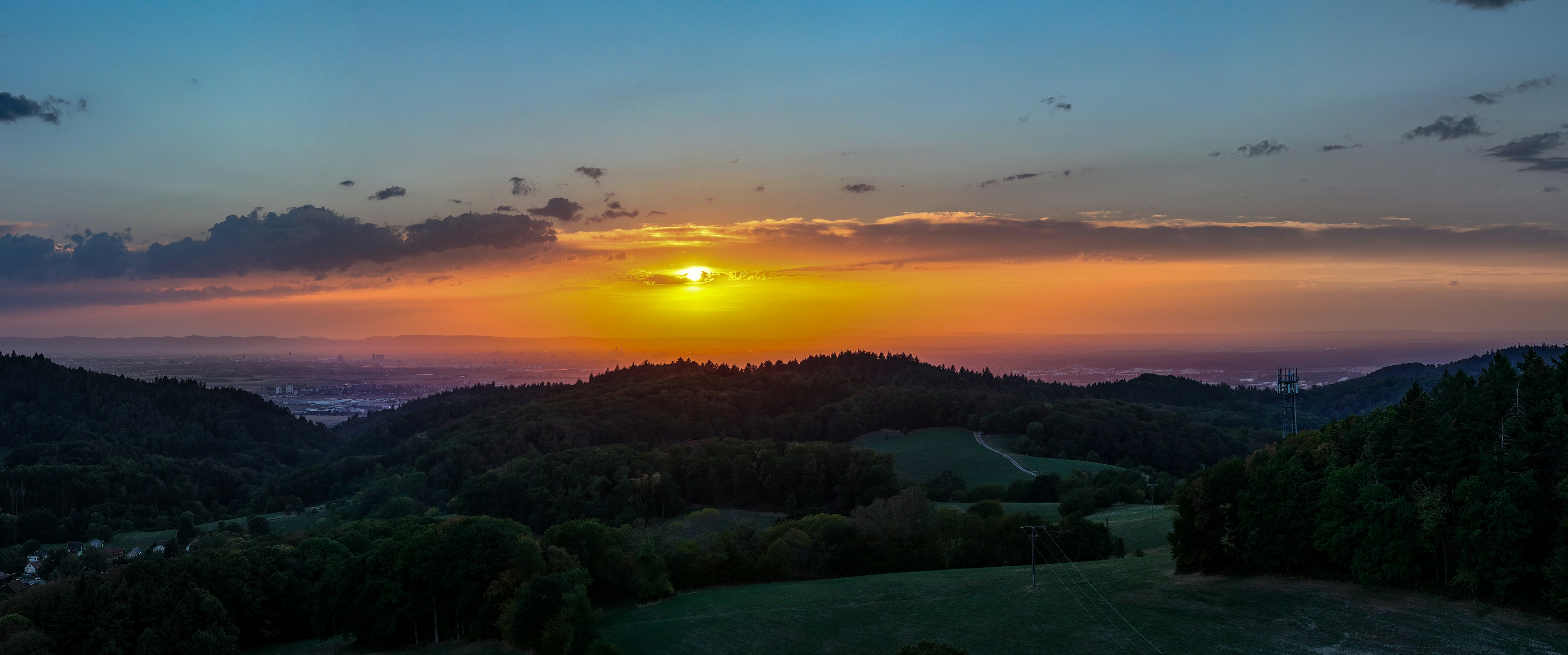 Low sun over a dark forested landscape with a distant hazy city