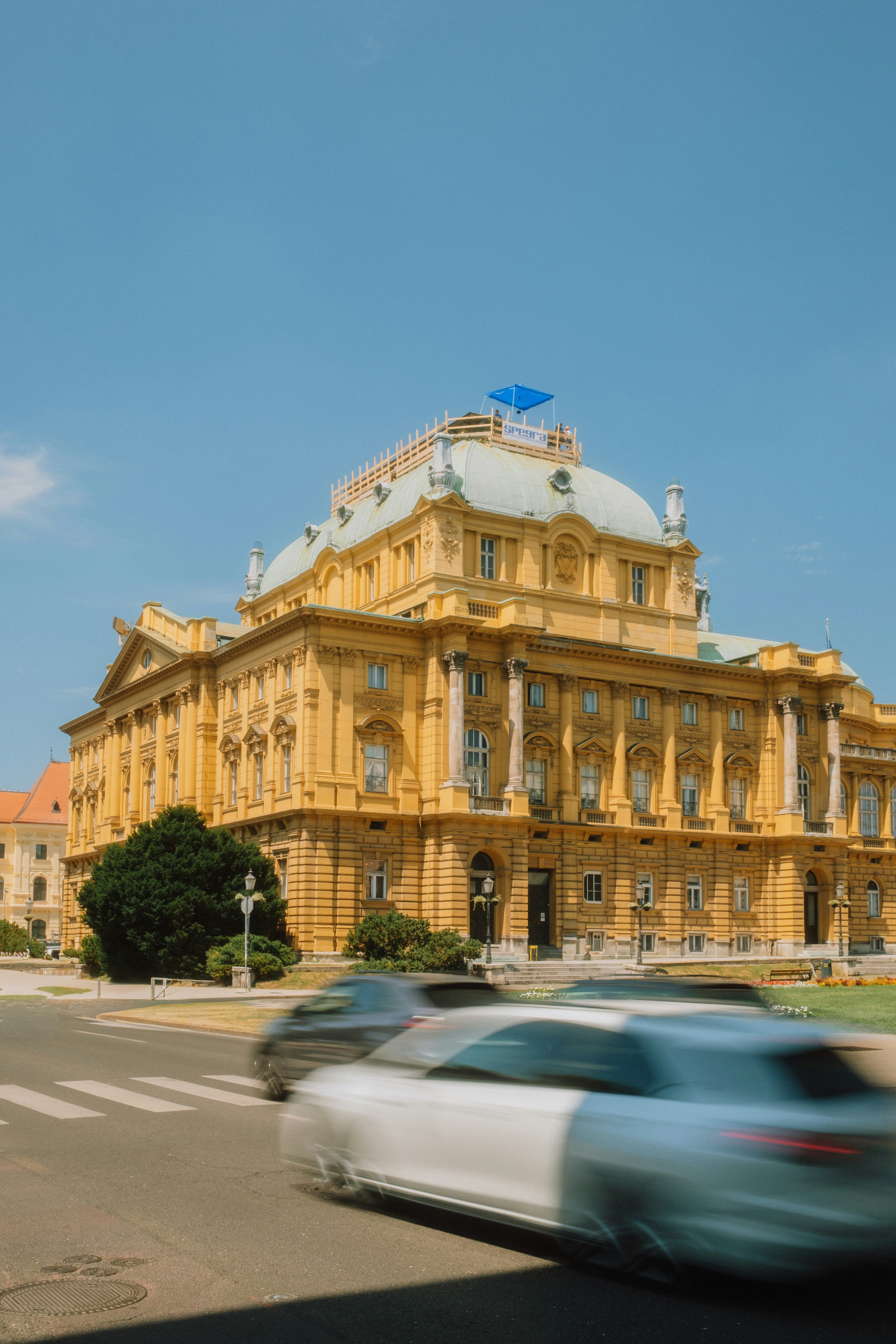 The yellow Croatian National Theatre in Zagreb with blurred cars passing in the foreground