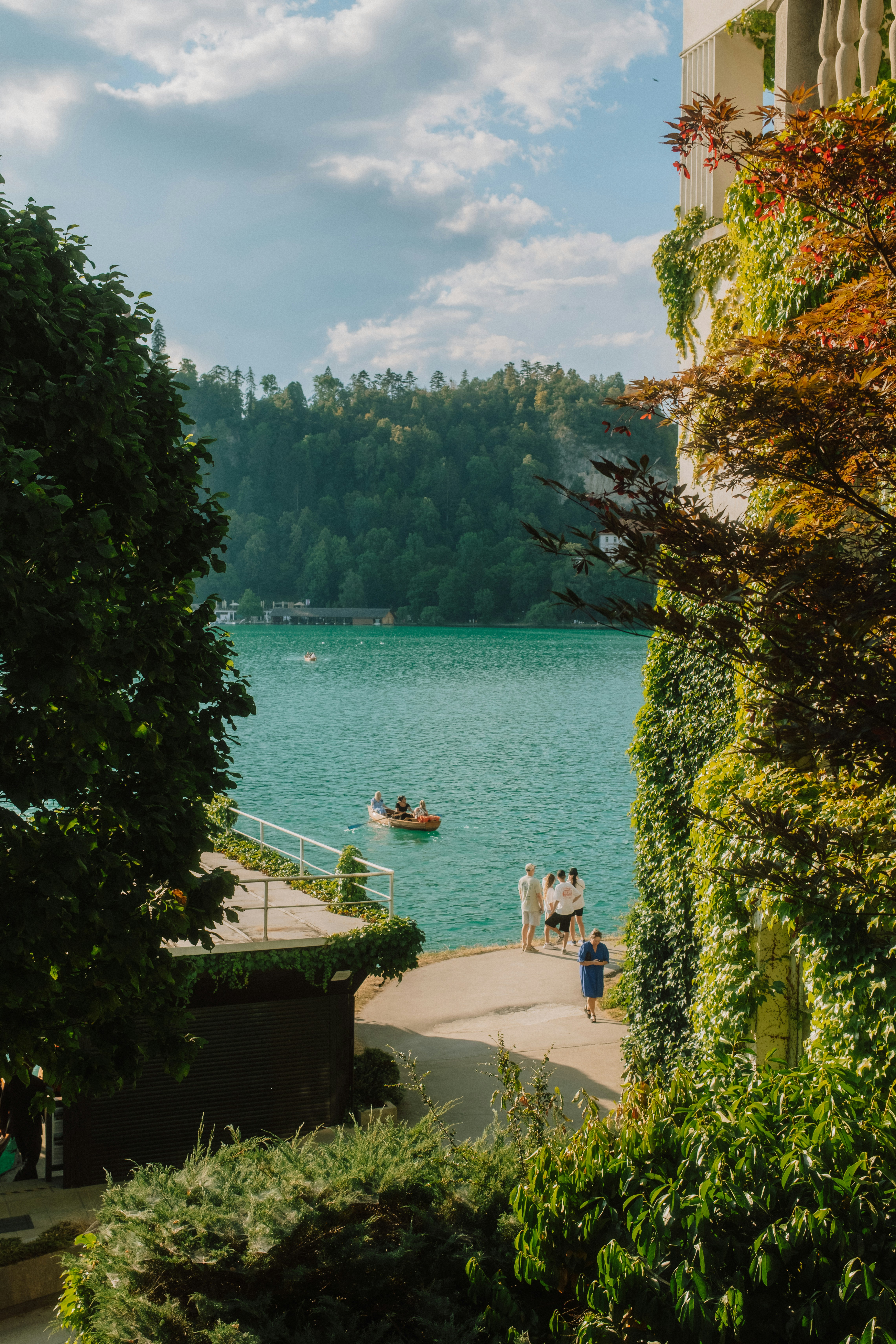 People on a path by a turquoise lake with a small wooden boat
