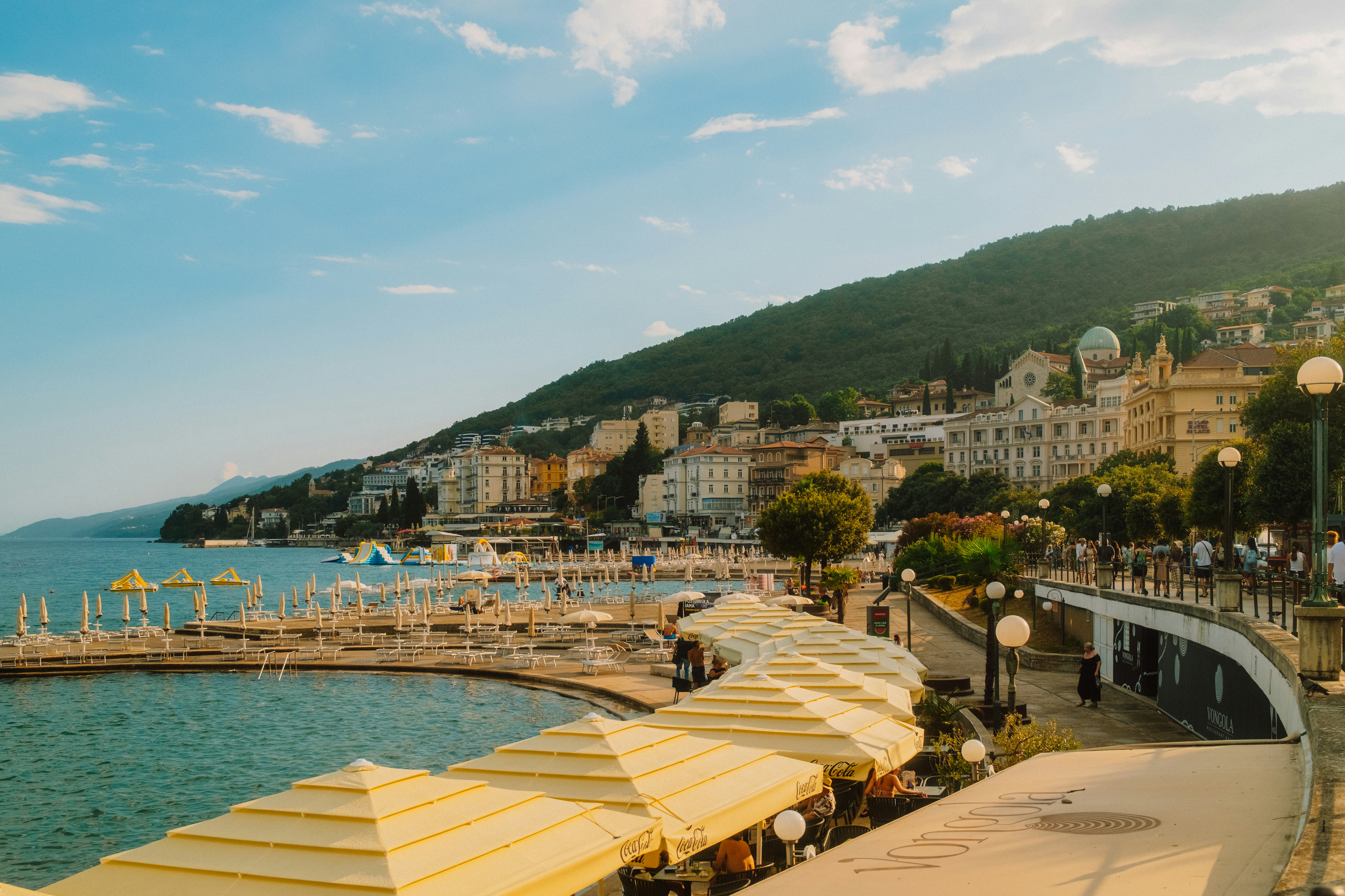 Yellow umbrellas along a coastal promenade with buildings on a hillside in Opatija